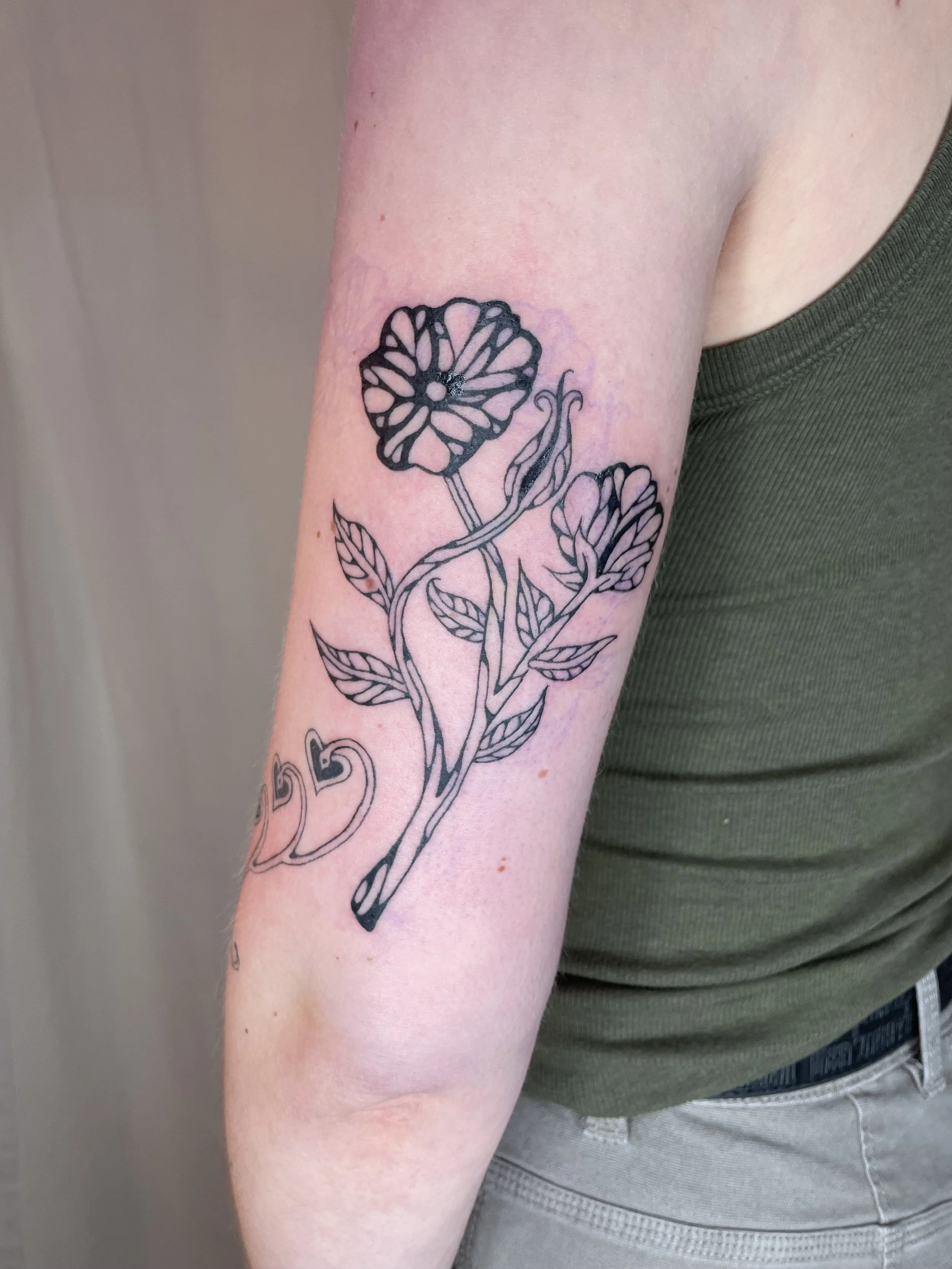 A tattoo of a stylized flower with leaves on a person's upper arm.