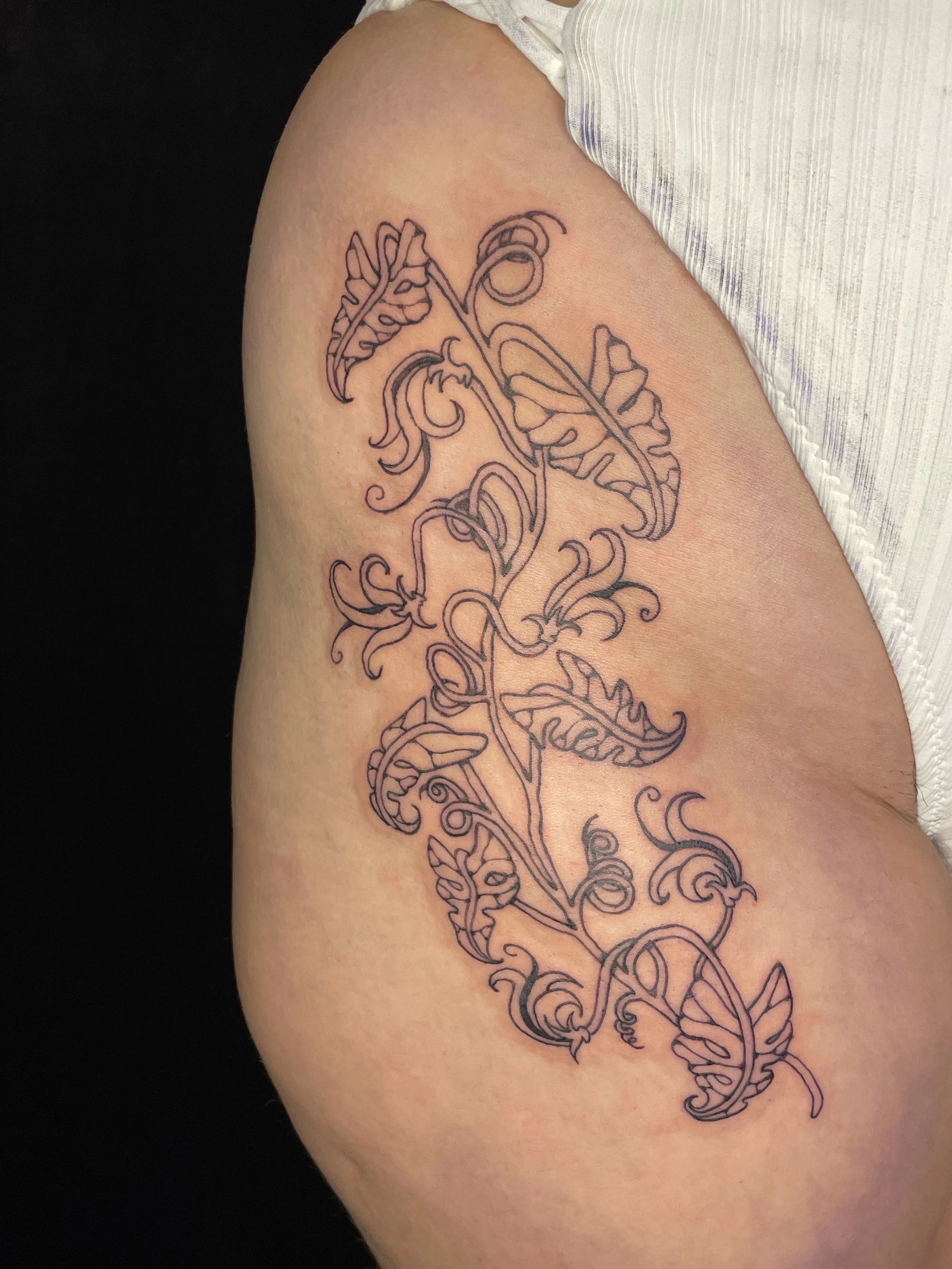 A tattoo of a stylized, intricate plant with leaves and swirling vines on a person's upper arm.