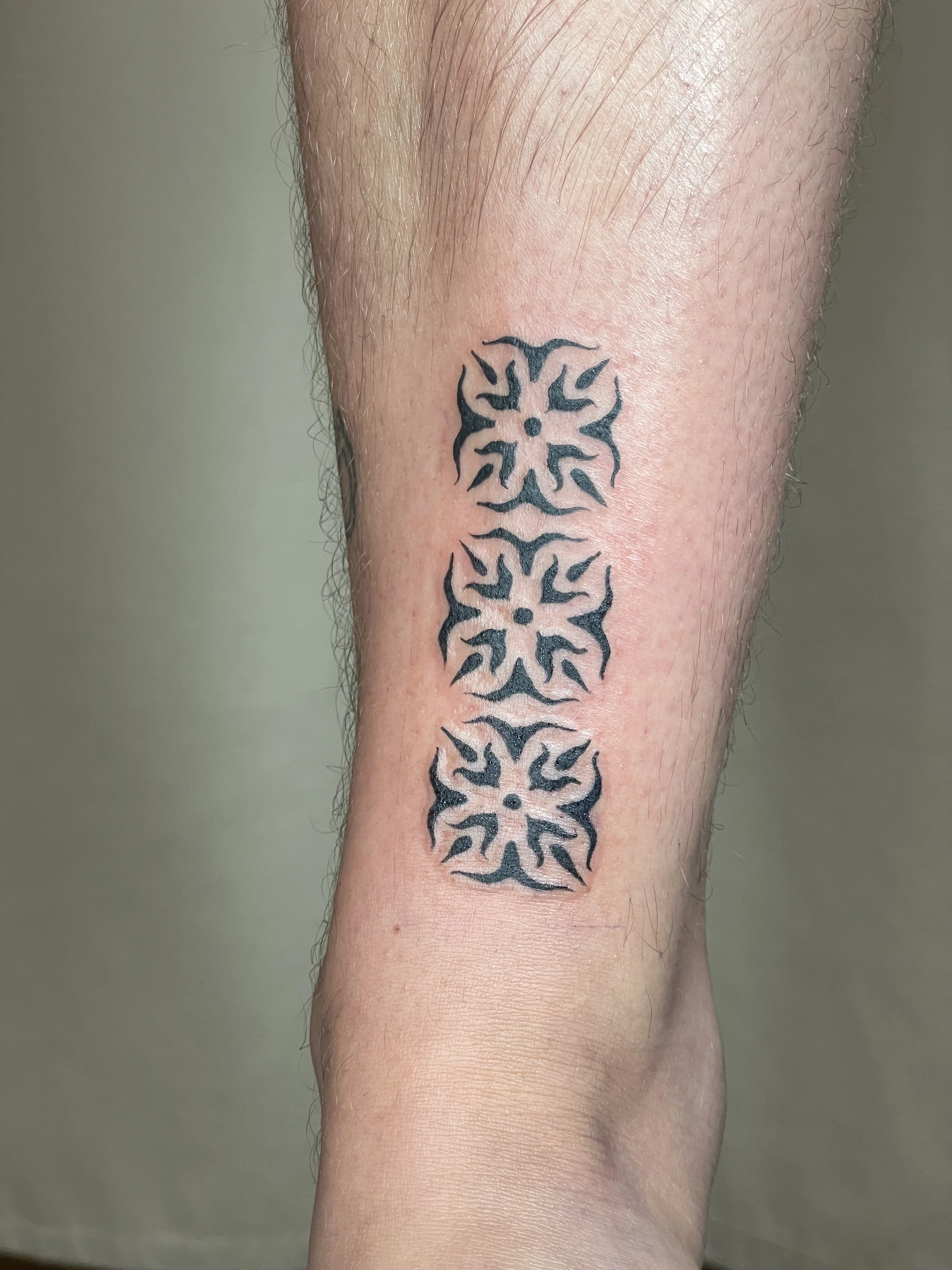 A person's calf with a black tribal-style tattoo of three symmetrical snowflake-like designs arranged vertically.