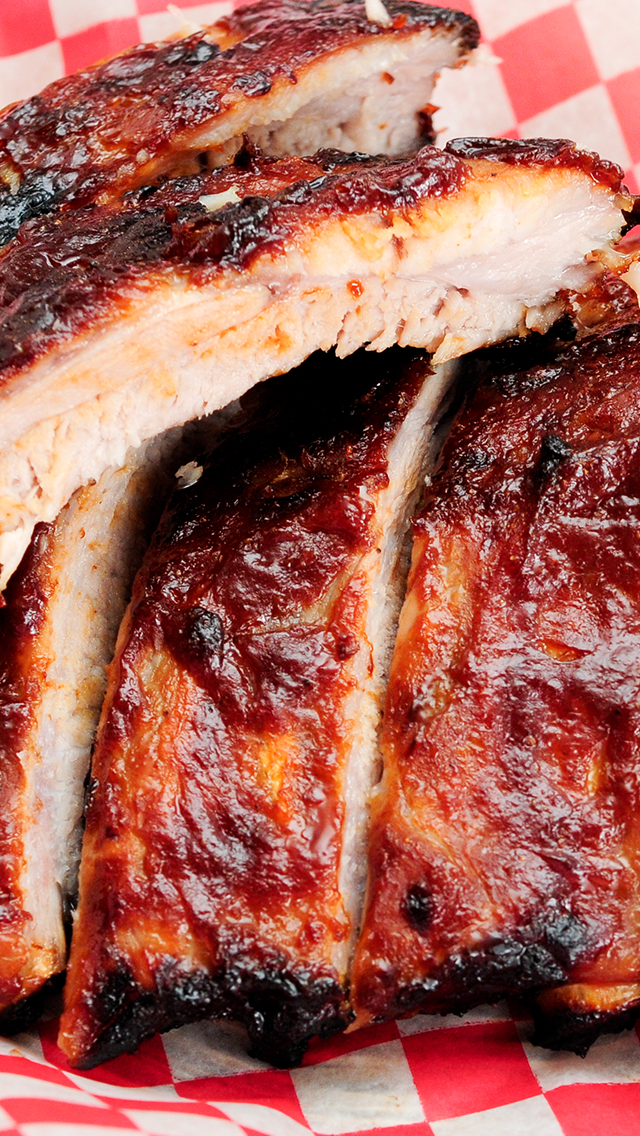 Close-up of barbecued chicken pieces with a crispy, glazed, caramelized exterior on red and white checkered paper.