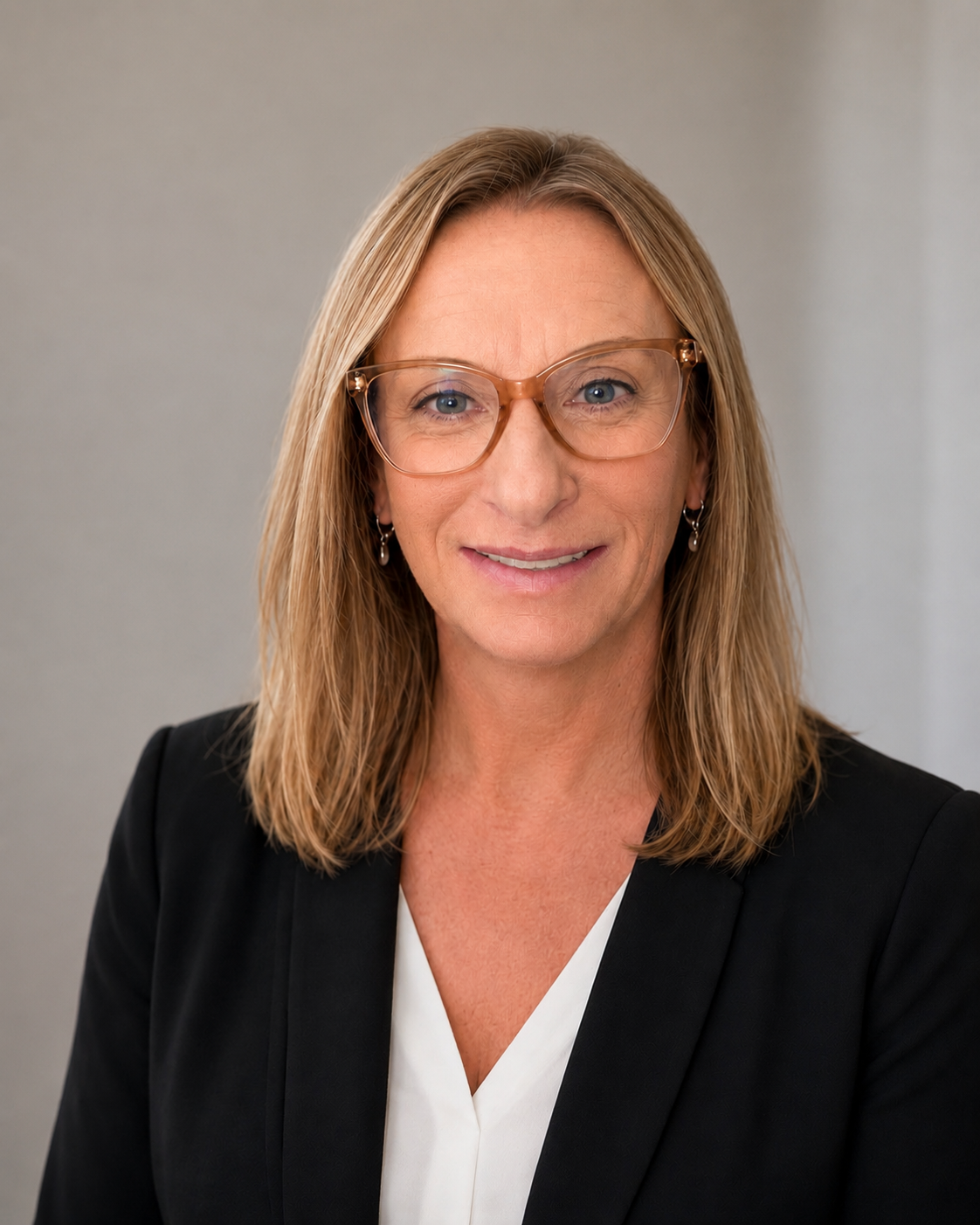 A professional woman with shoulder-length blond hair, wearing glasses, earrings, a black blazer, and a white blouse, smiling at the camera against a plain background.