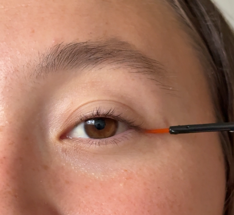 Close-up of a person's eye with makeup brush applying eyeshadow or eyeliner.