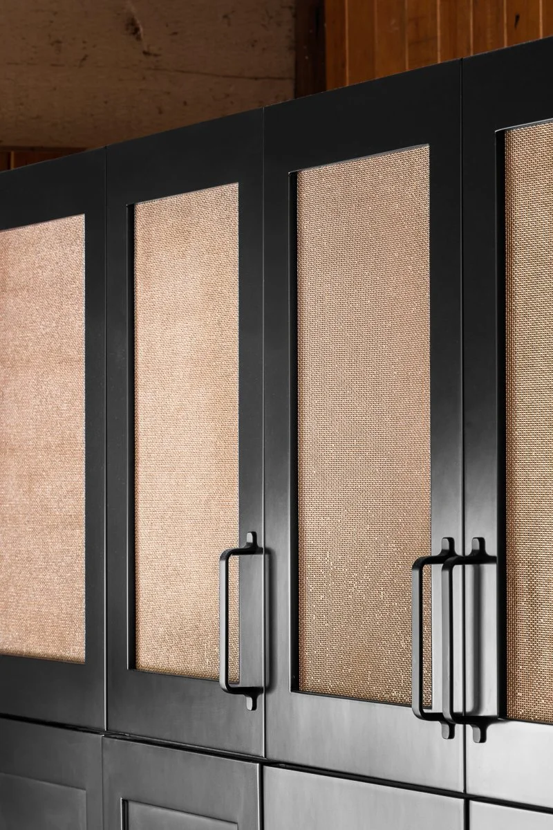 Close-up of black kitchen cabinet doors with textured copper mesh and black handles.