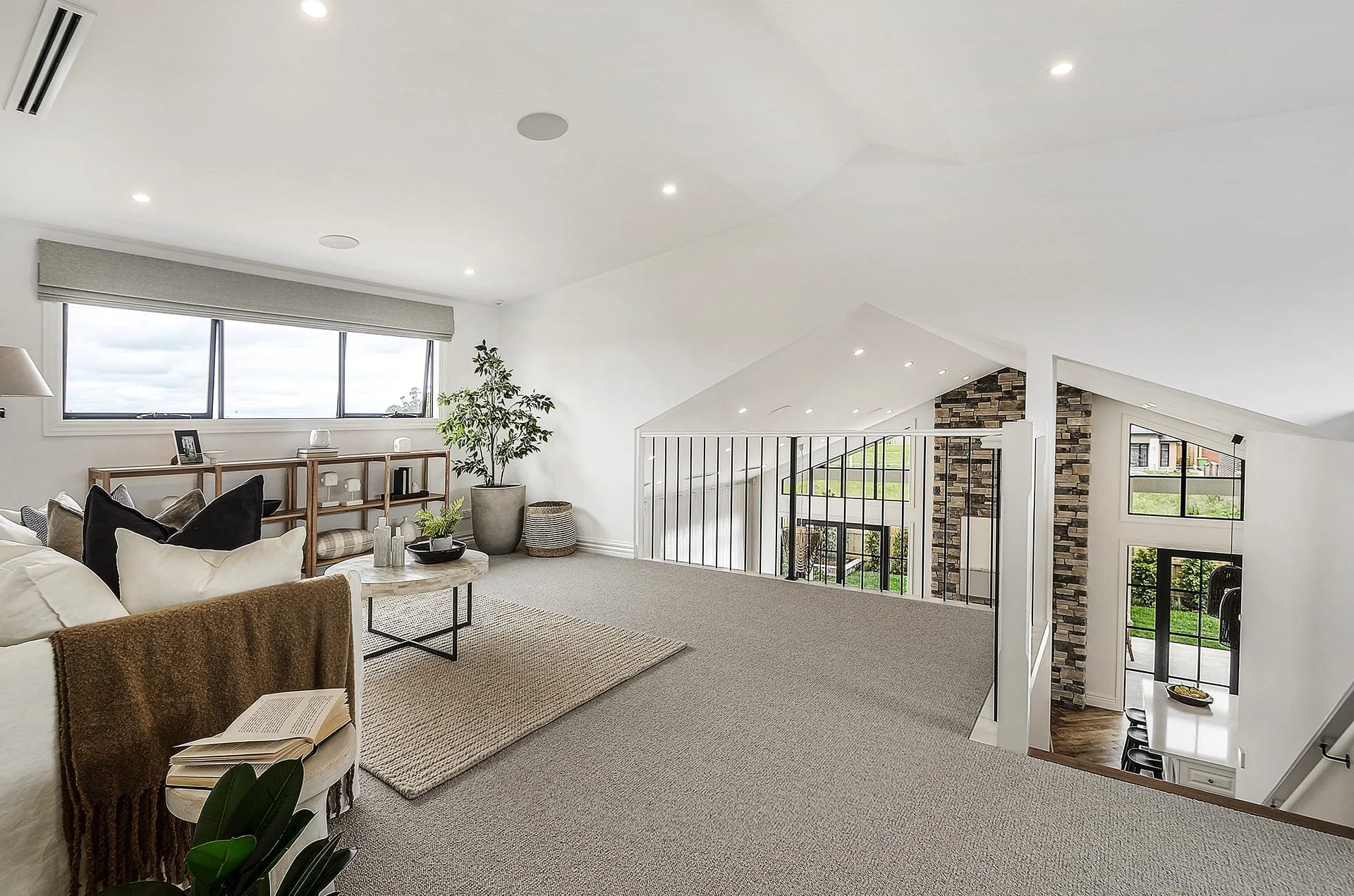 An open retreat area in an attic space with a raked ceiling, overlooking a spacious open living area below.