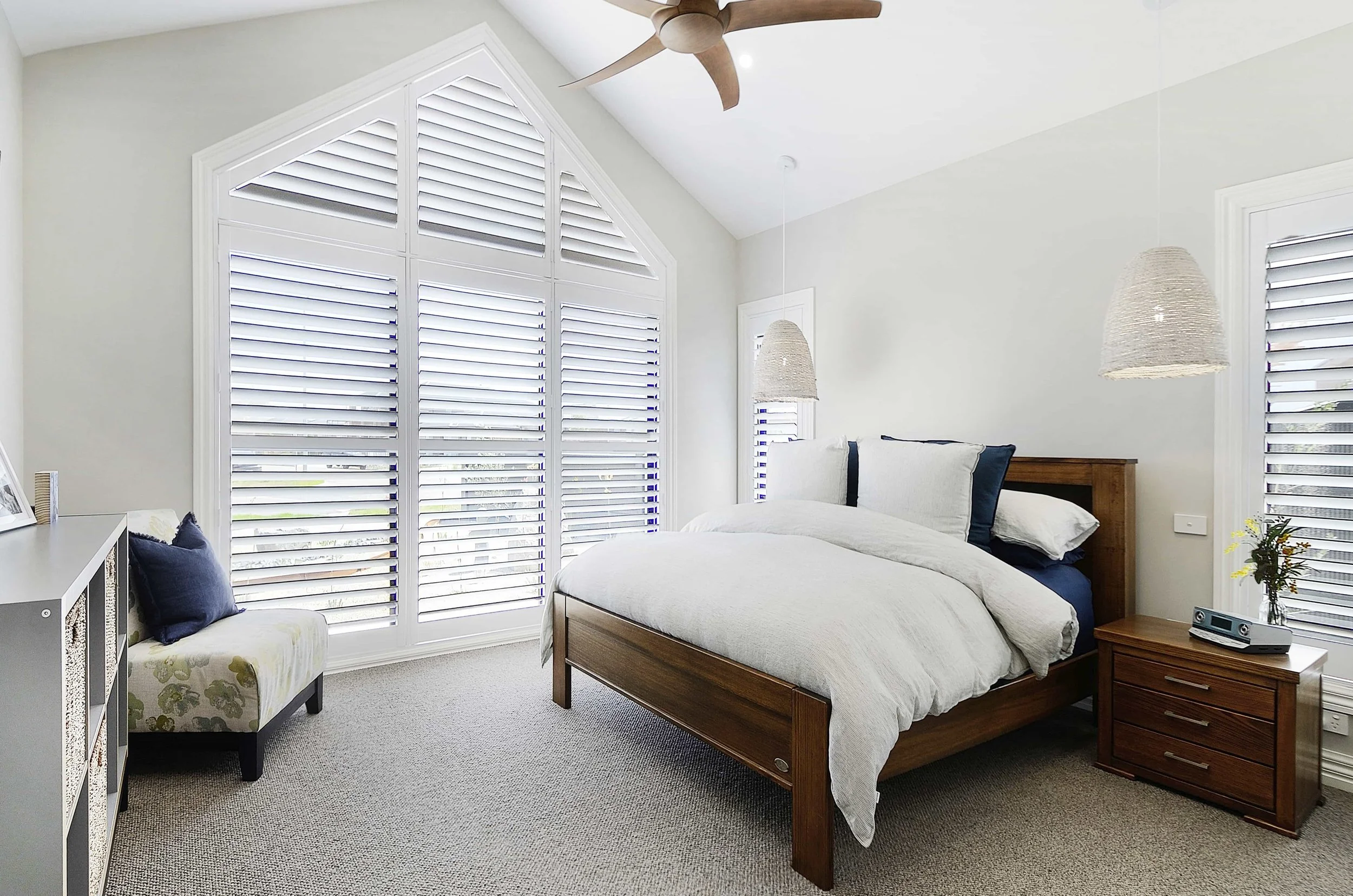 A bedroom with a large trapezoid window in a room with a square set cathedral ceiling.