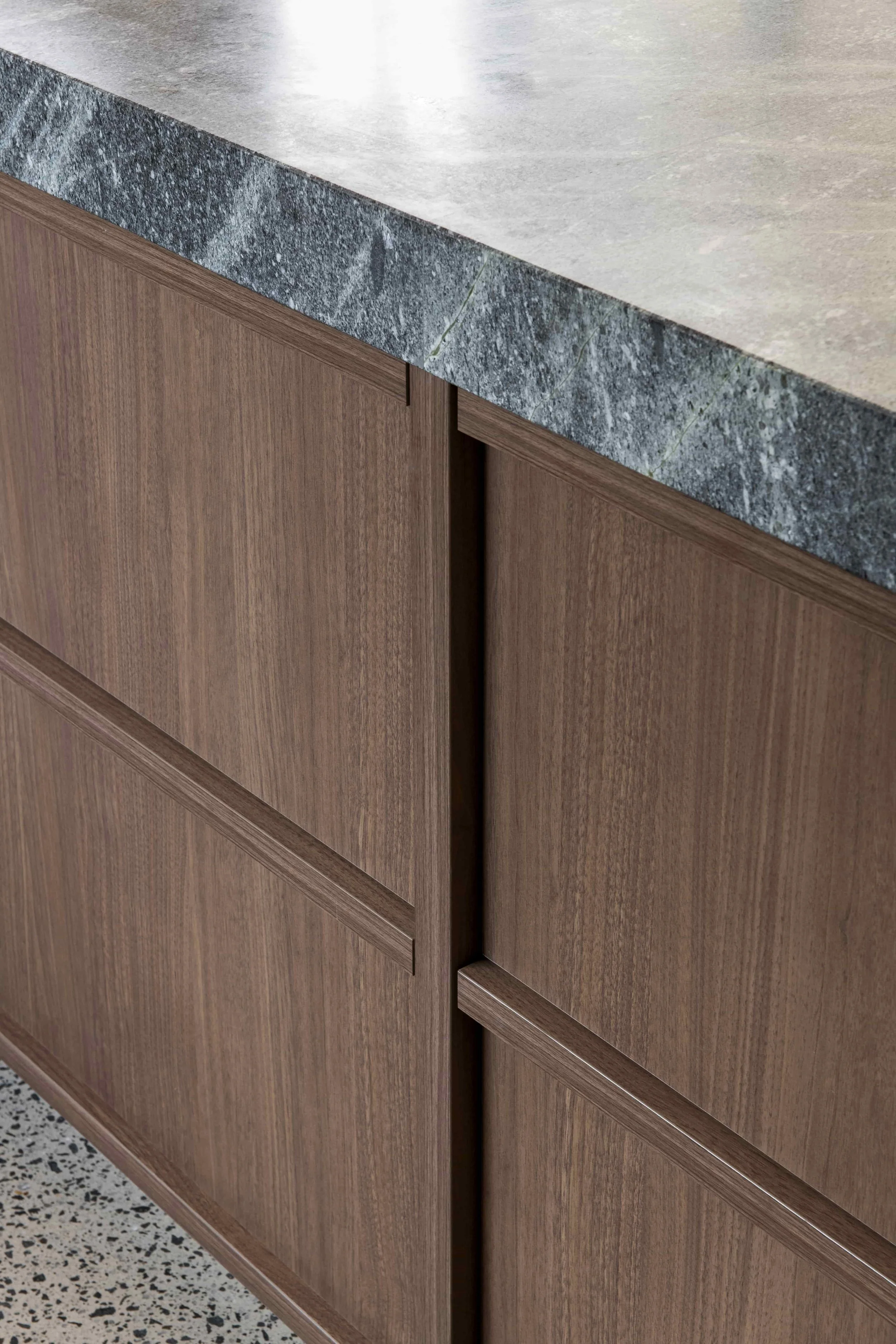 A close-up of custom timber cabinet doors with a thick grey stone benchtop above them.