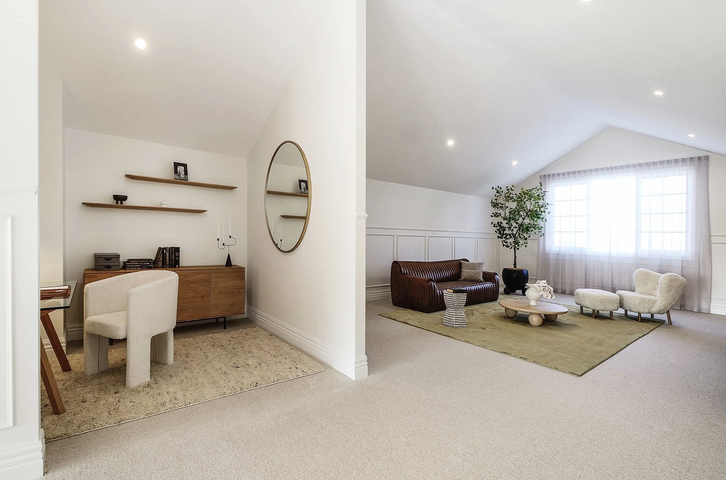 Attic rumpus with high cathedral ceiling, large colonial windows with sheer curtains, a breakout study corner, a potted plant, a brown leather sofa, a white curved armchair, a small round wooden coffee table, and a green area rug.