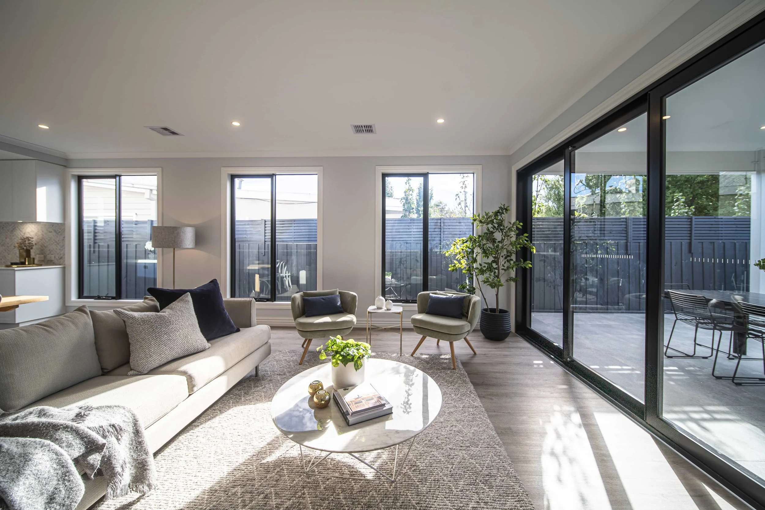 A modern open living room with ample natural light the space. The large black framed sliding doors to the right lead to an undercover alfresco area.