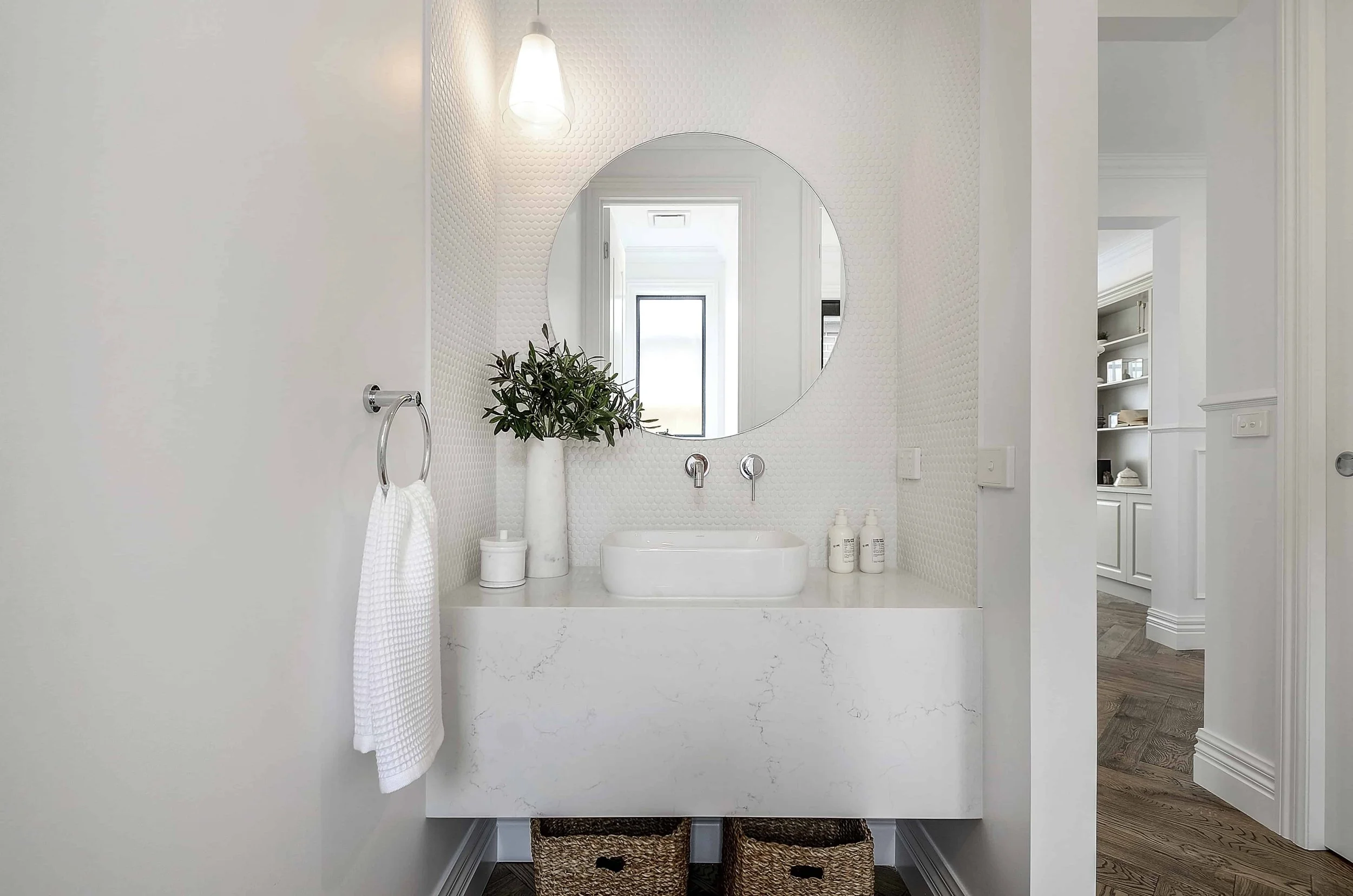 Modern powder room with a floating white stone vanity, round mirror, above counter basin, and a white round penny tile splashback going to the ceiling.
