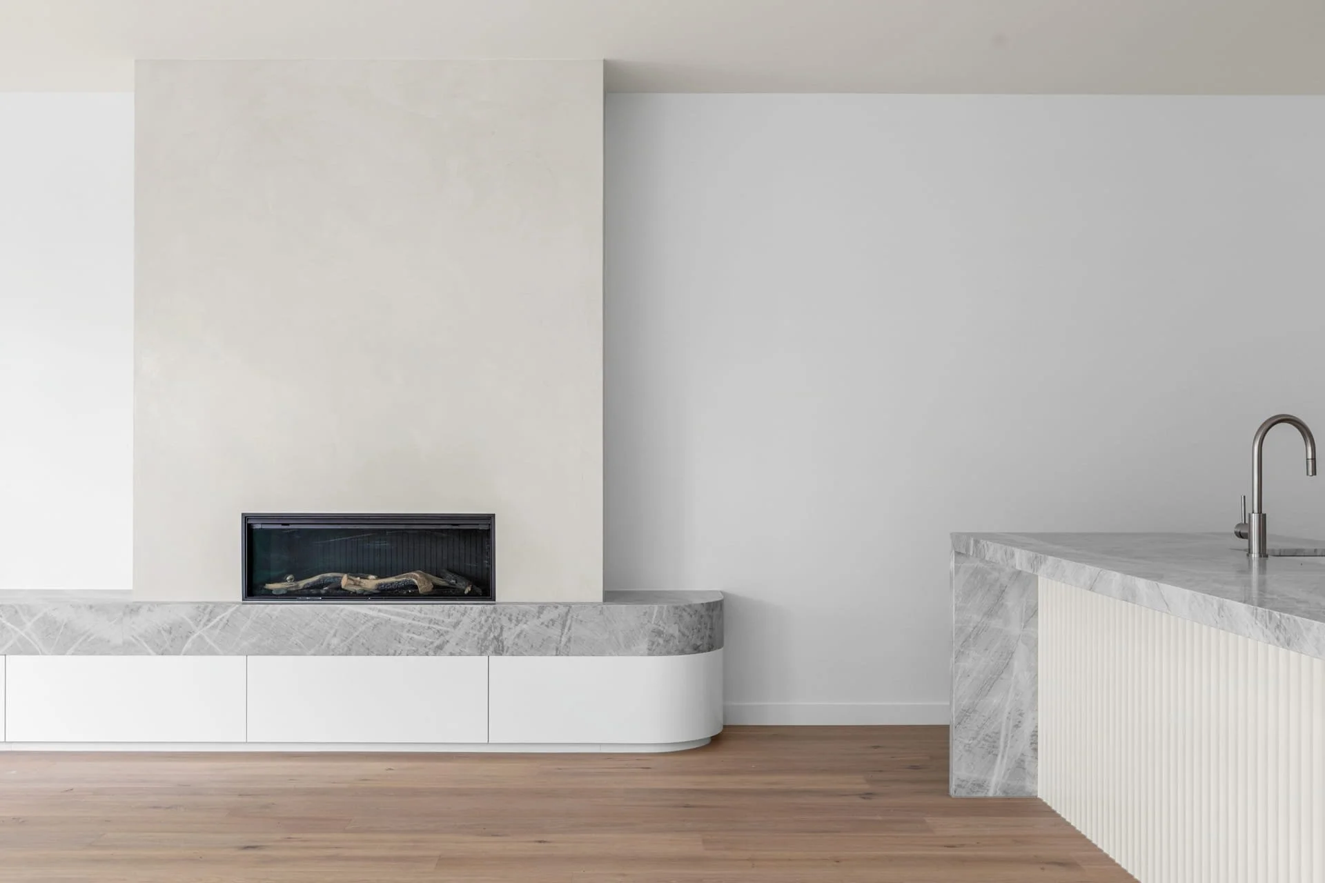 Minimalist living space with a modern rendered fireplace and a kitchen island with a waterfall edge finish.