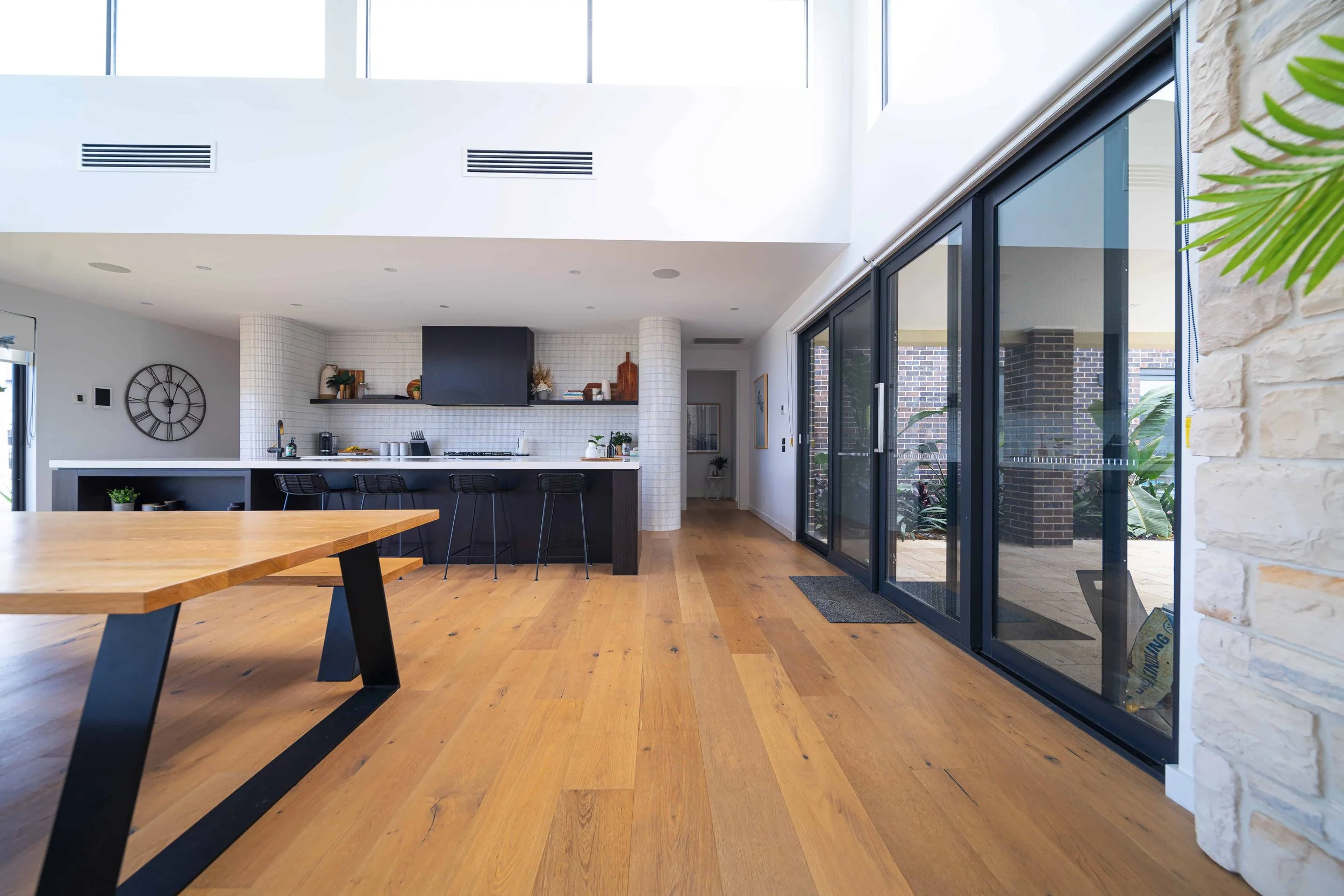 Modern open-concept kitchen and living area with large sliding glass doors, wooden flooring, white walls, and contemporary furniture decorations.