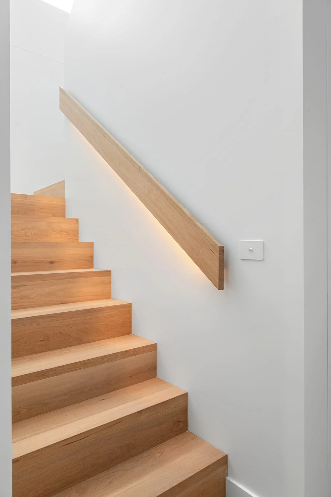 Timber staircase with a simple wooden handrail on a white wall.