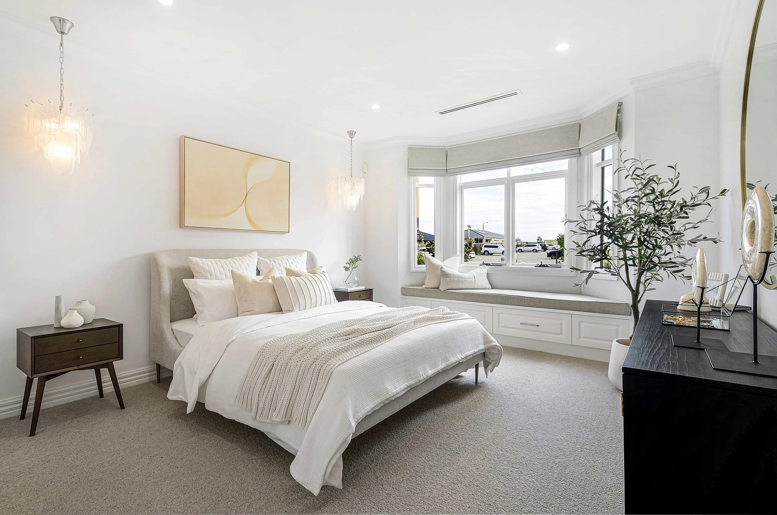 A bright master bed suite with a feature bay window looking to the street. The bay window has seating below with built in storage. There are feature pendant lights over the bedside tables and abstract art above the bed.