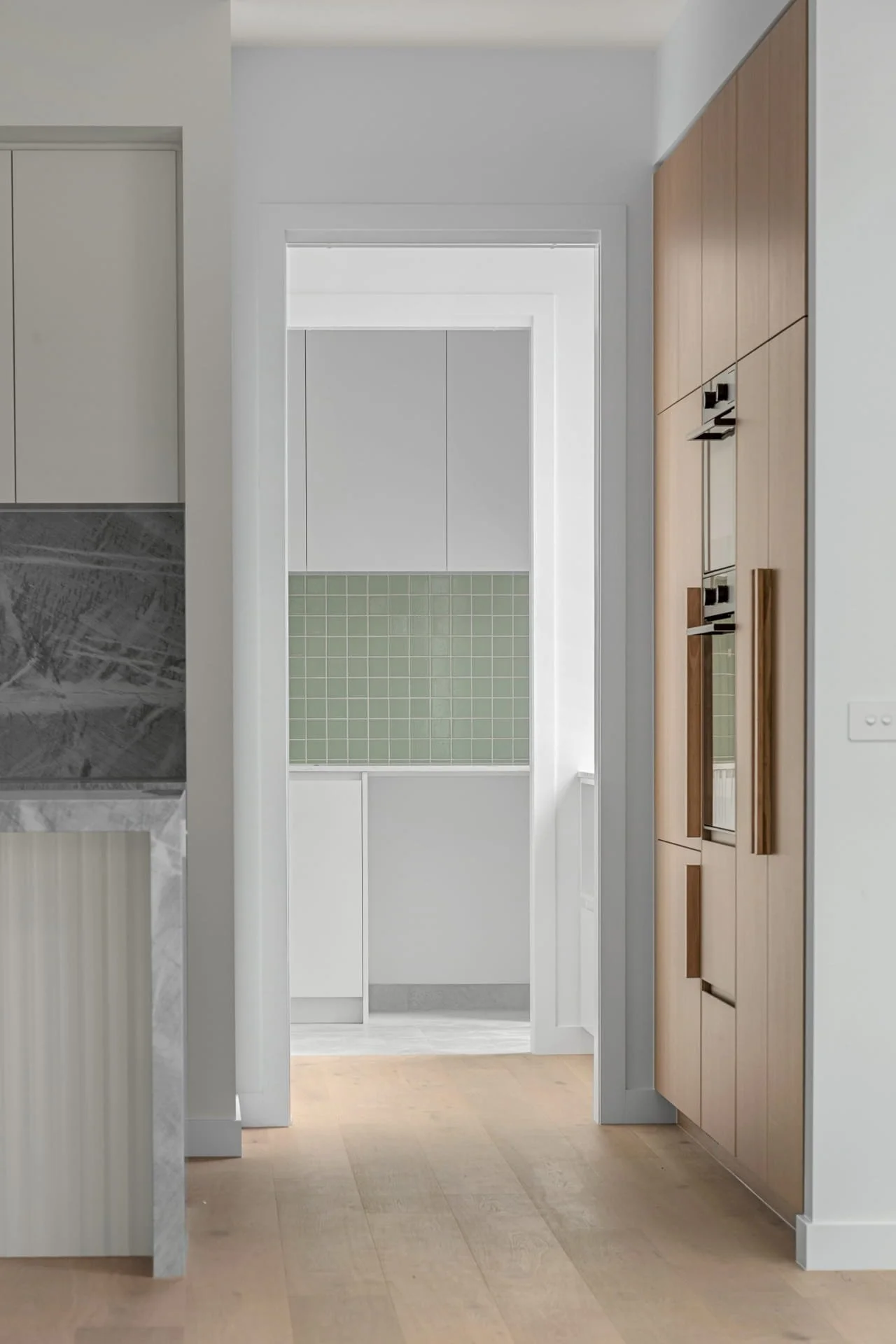 View through a kitchen doorway into a room with white cabinetry and green mosaic tiled walls.
