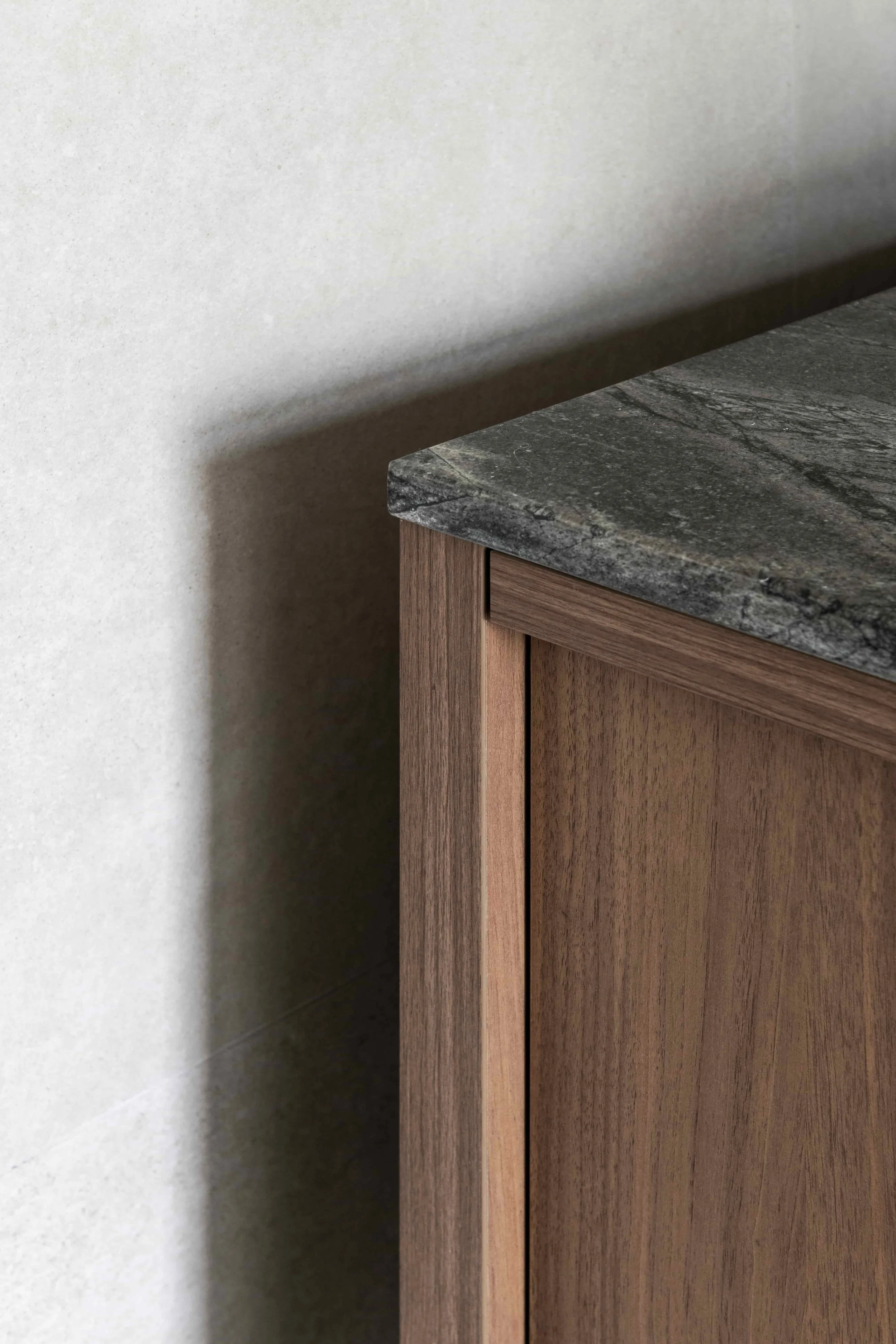 Close-up detail of a corner of a timber cabinet with a grey stone benchtop against a plain wall.