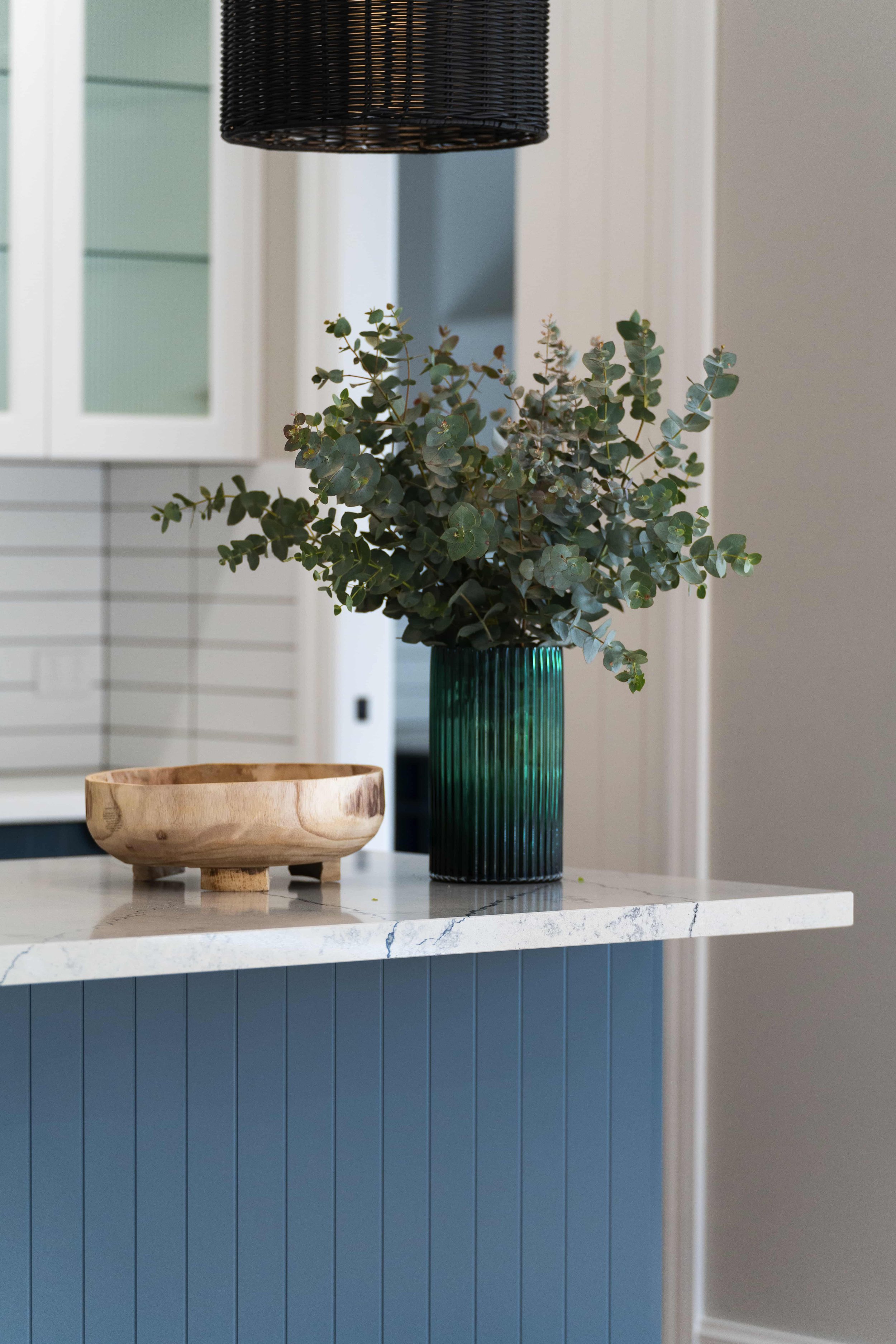 A kitchen island with blue routed cabinet panels and a white benchtop with grey veins.