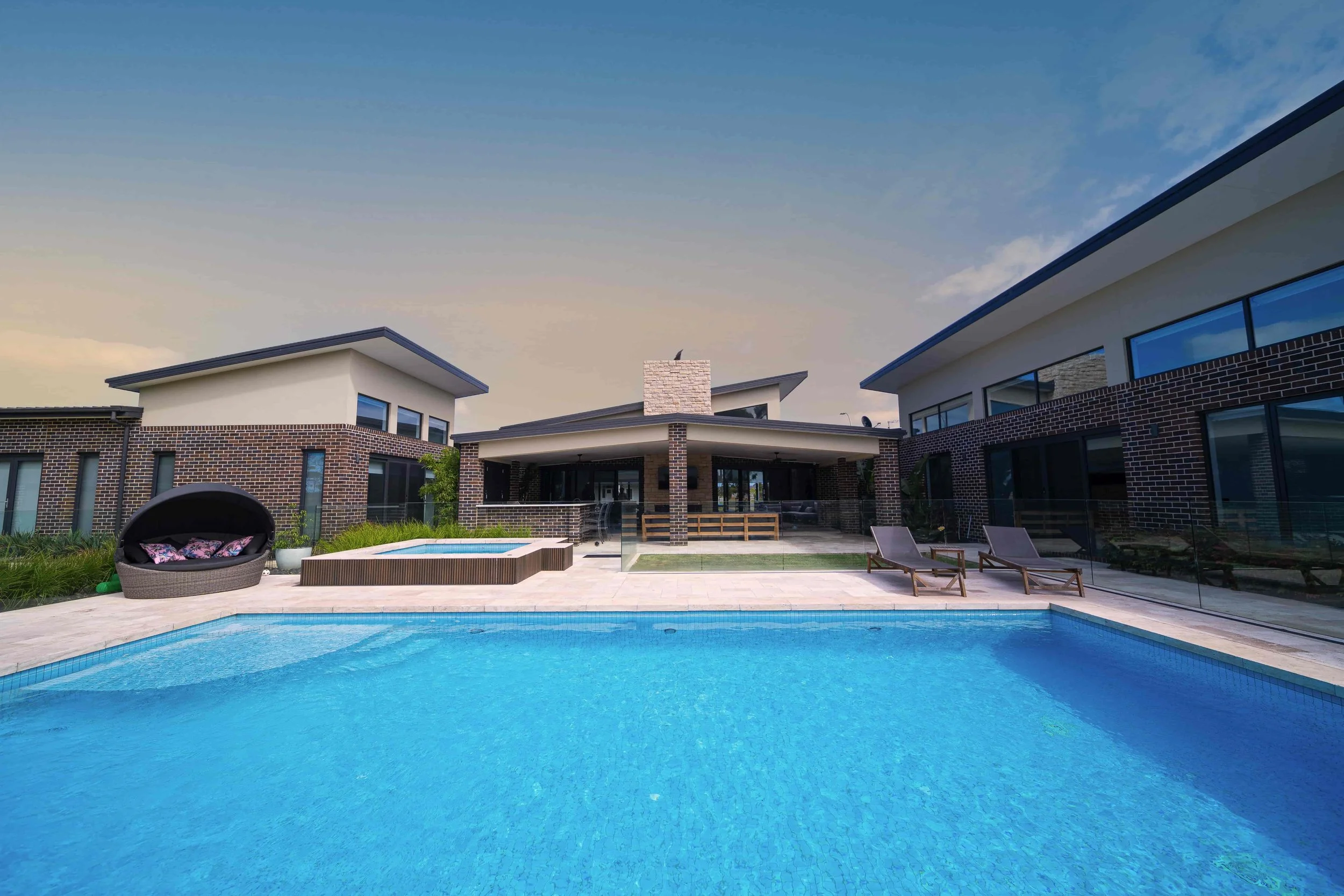 Modern house with a backyard pool, raised spa, outdoor seating, and lounge chairs under a blue sky.