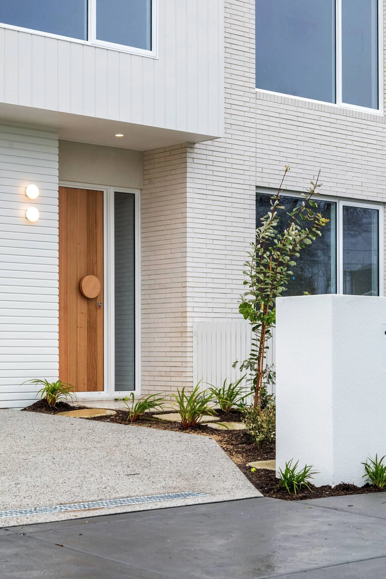 A house façade with modern white bricks and a feature timber entry door.