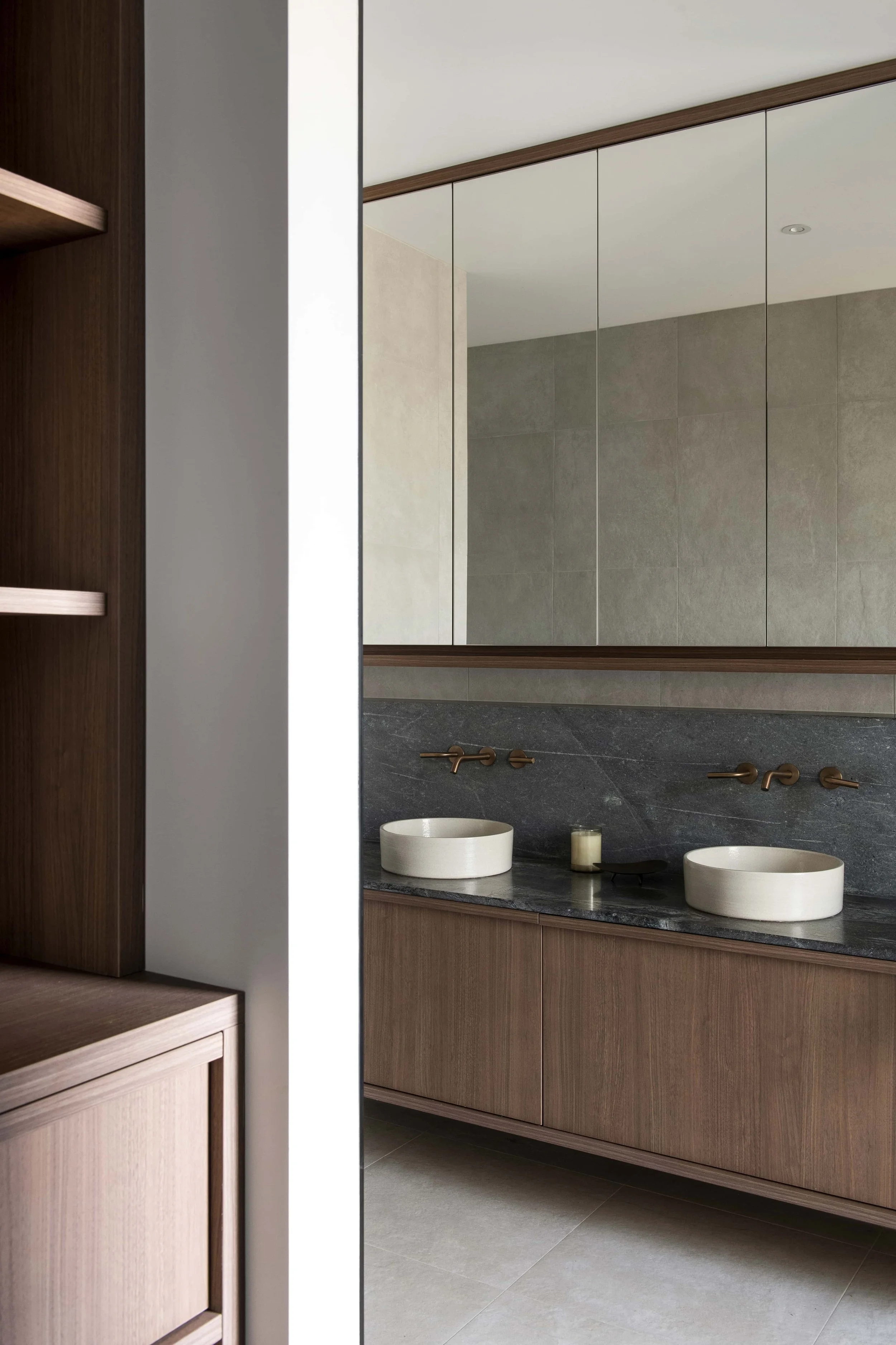 Modern ensuite with floating vanity, dark grey stone benchtops and splashback, and two round above bench basins, with bronze fixtures and a large mirror.
