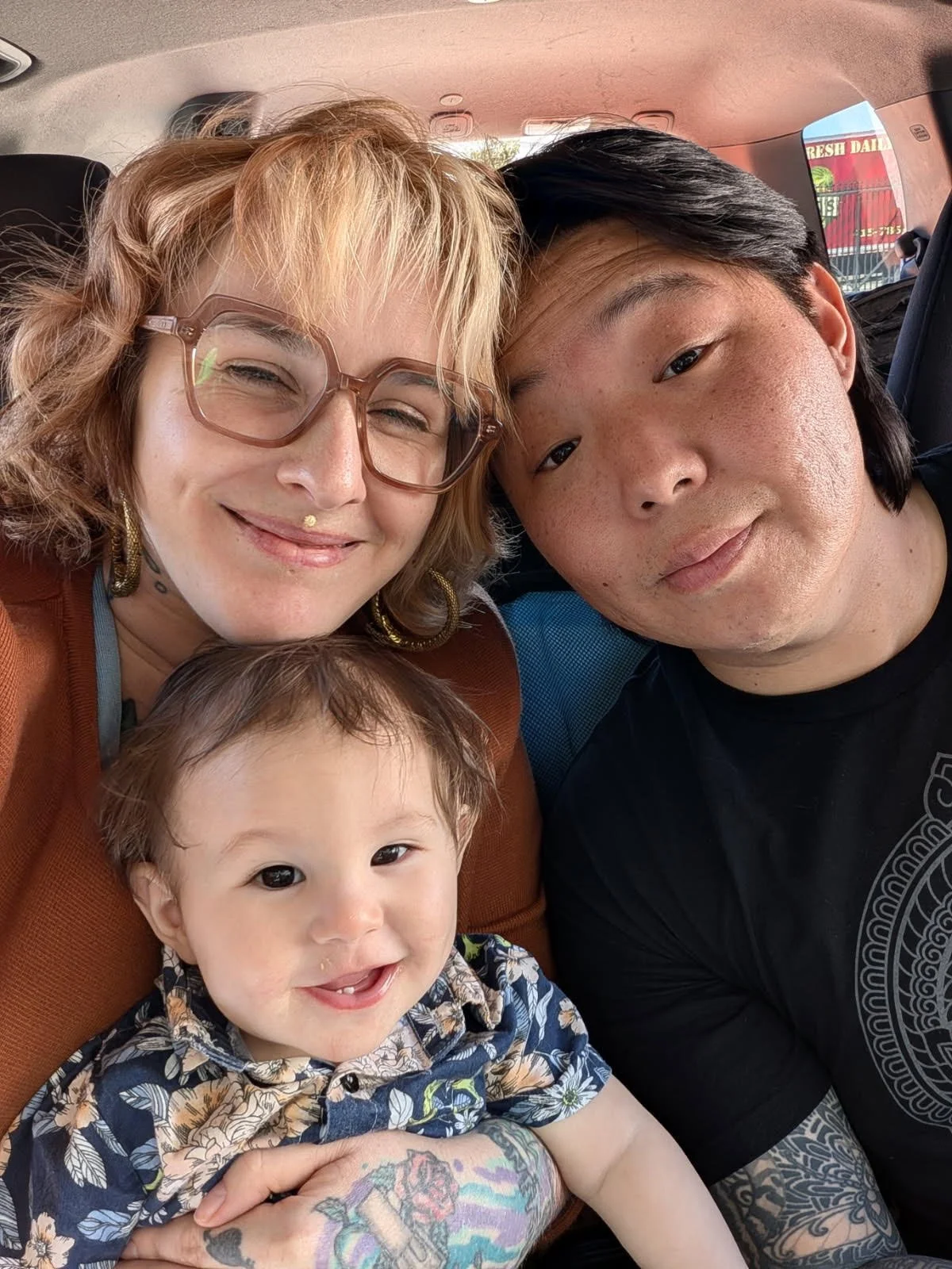 A group of four people, including two adults and two children, taking a selfie inside a vehicle. They are smiling and looking at the camera.