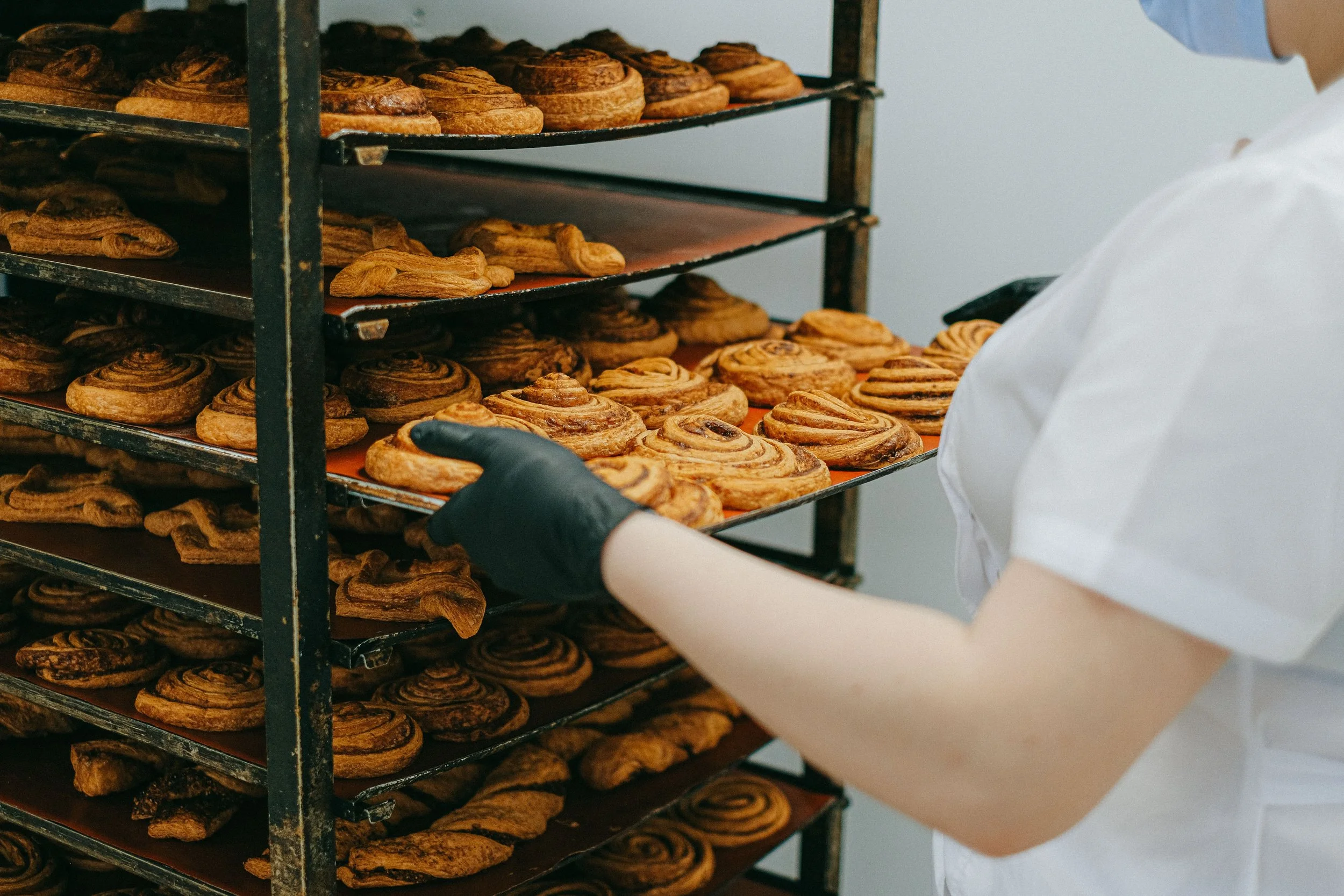 Bakery worker handling freshly baked cinnamon rolls on a rack.