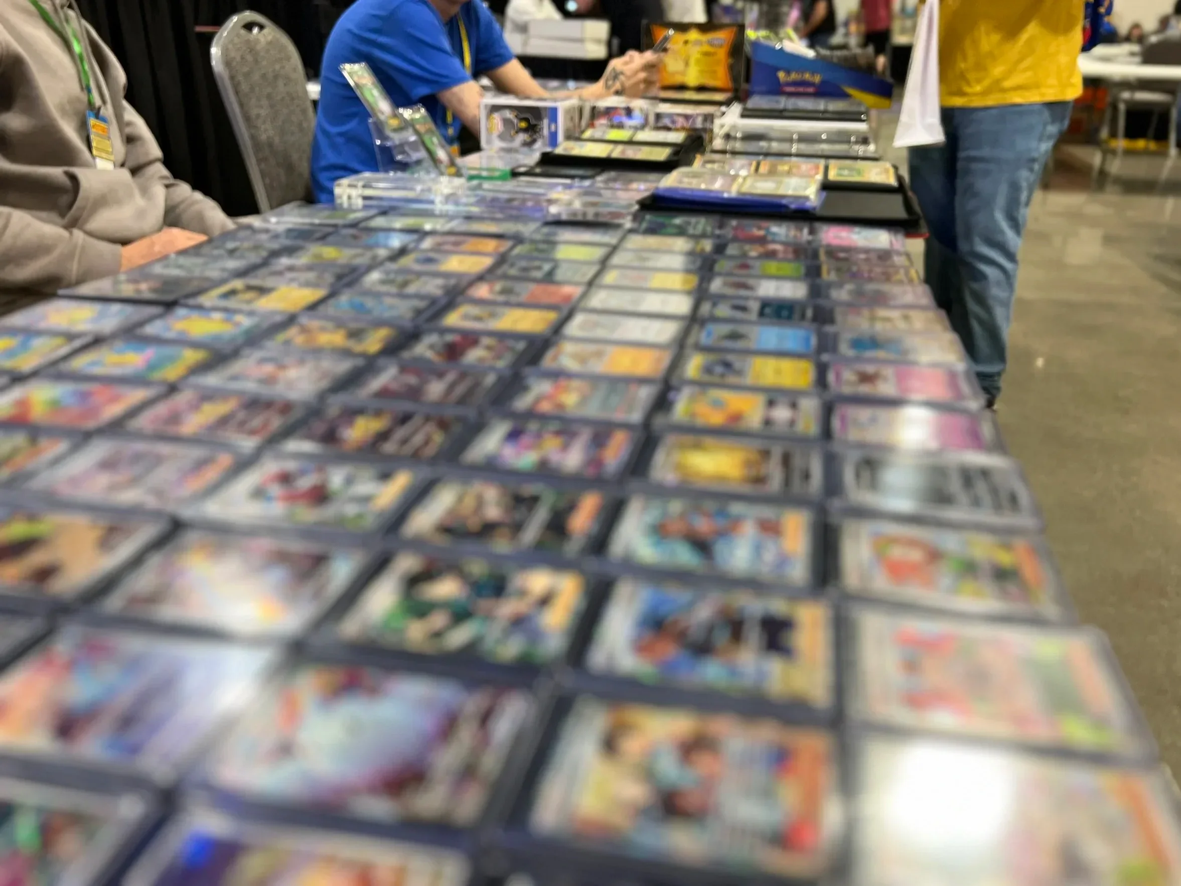 A table filled with trading cards displayed in plastic sleeves at a convention or card show.