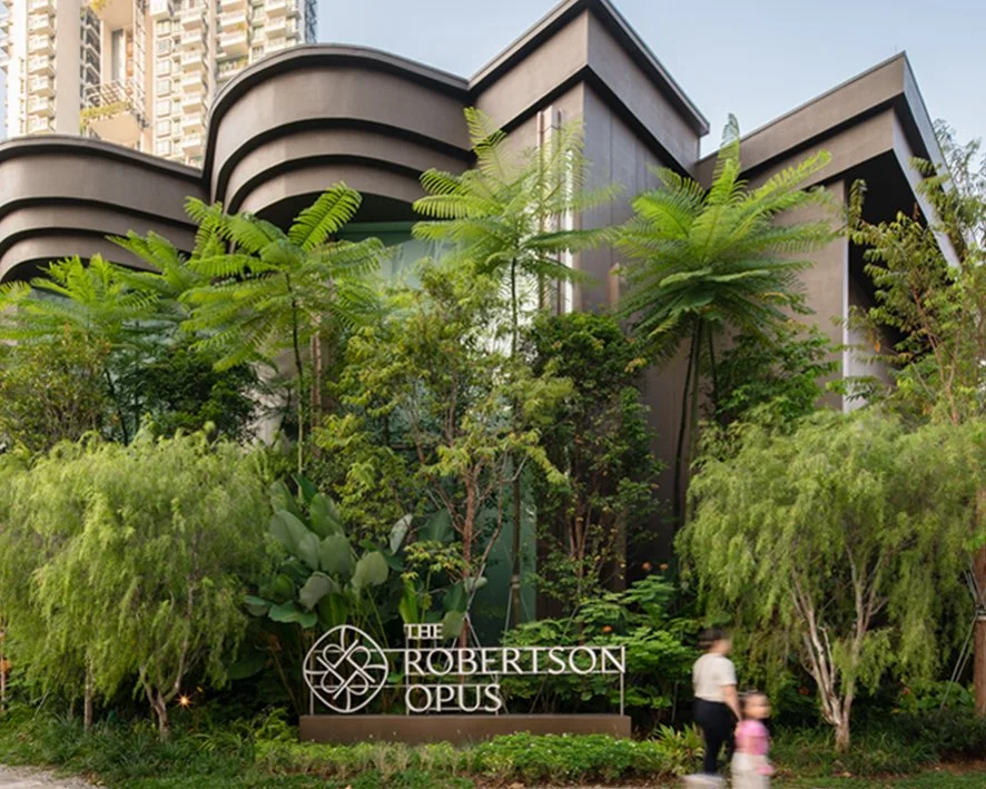 Modern building with curved roof design surrounded by lush green trees and plants, with a sign that reads 'The Robertson Opus' at the front.