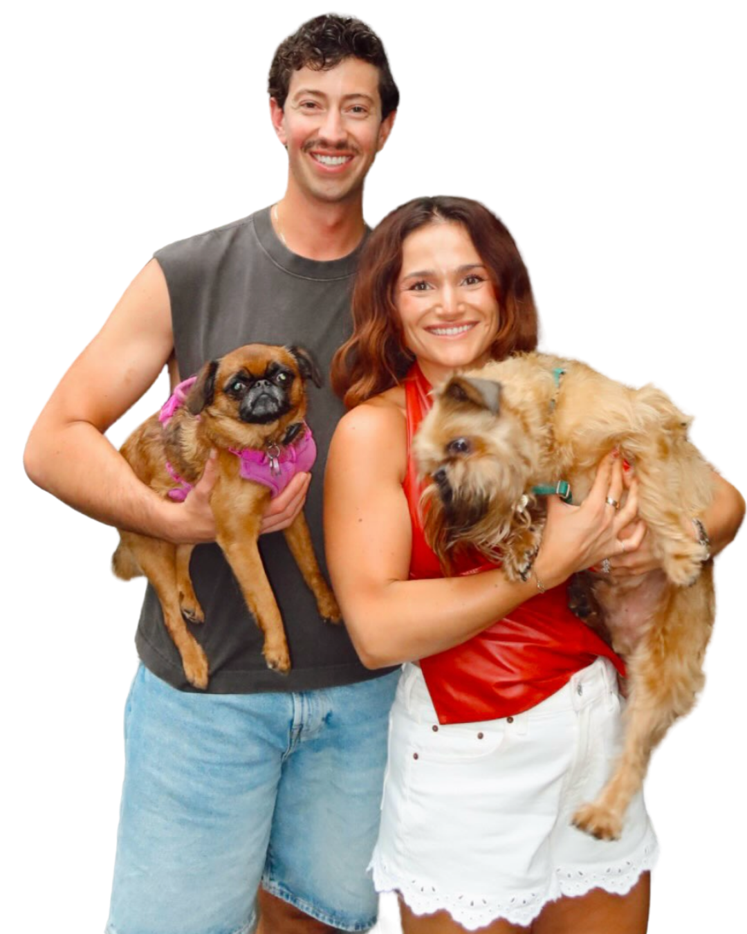 Smiling man and woman holding two small dogs, one wearing a pink harness, against a plain background.