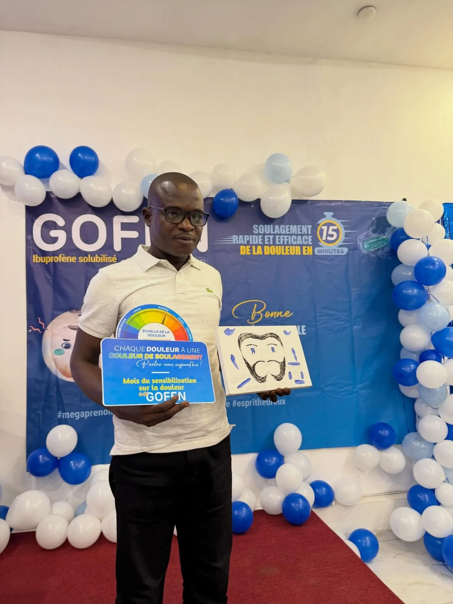Man holding a sign and a drawing at health awareness event with blue and white balloons and promotional banner in background.