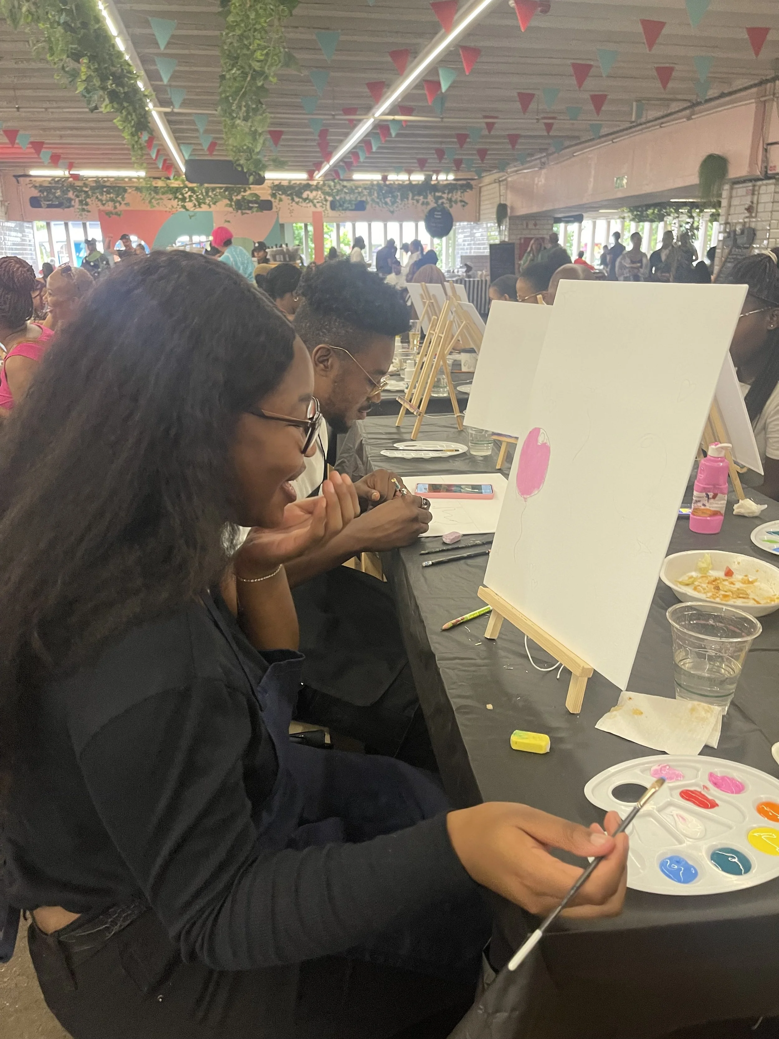 People at a paint and sip event, painting on canvases with palettes of colorful paints in a decorated indoor space.