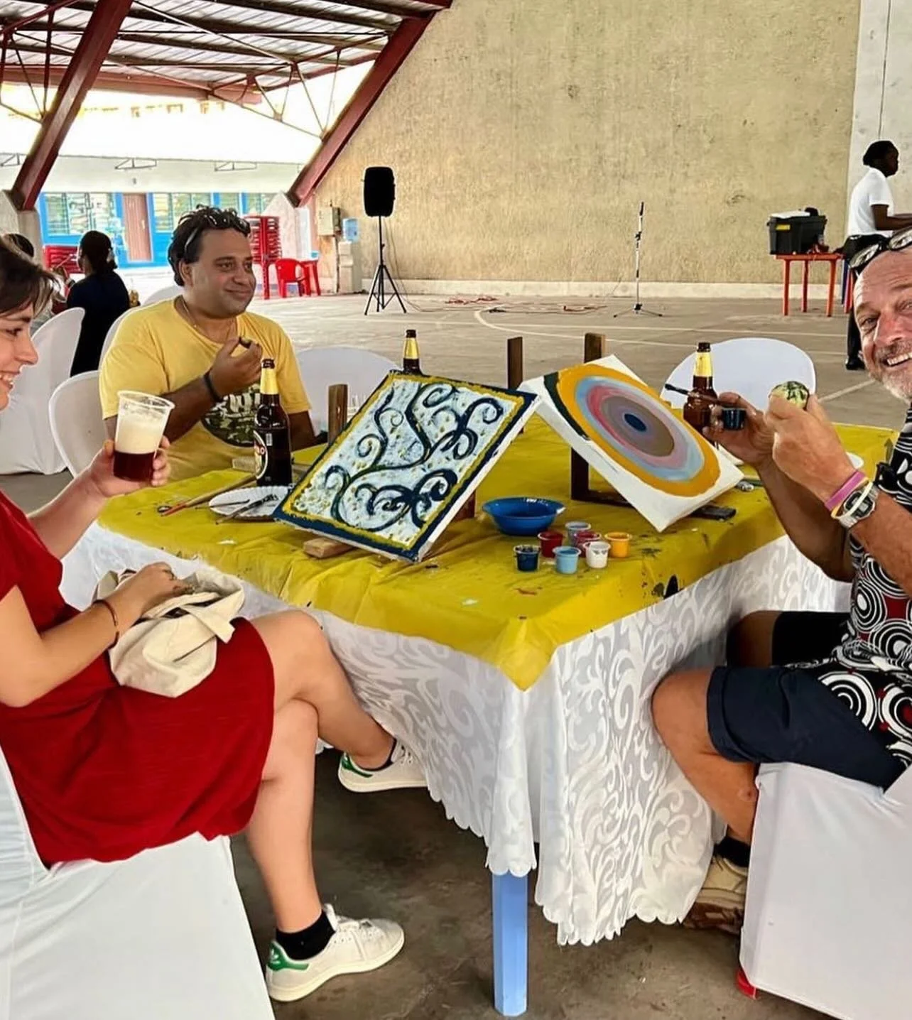 People painting and enjoying drinks at a table under a covered outdoor space.