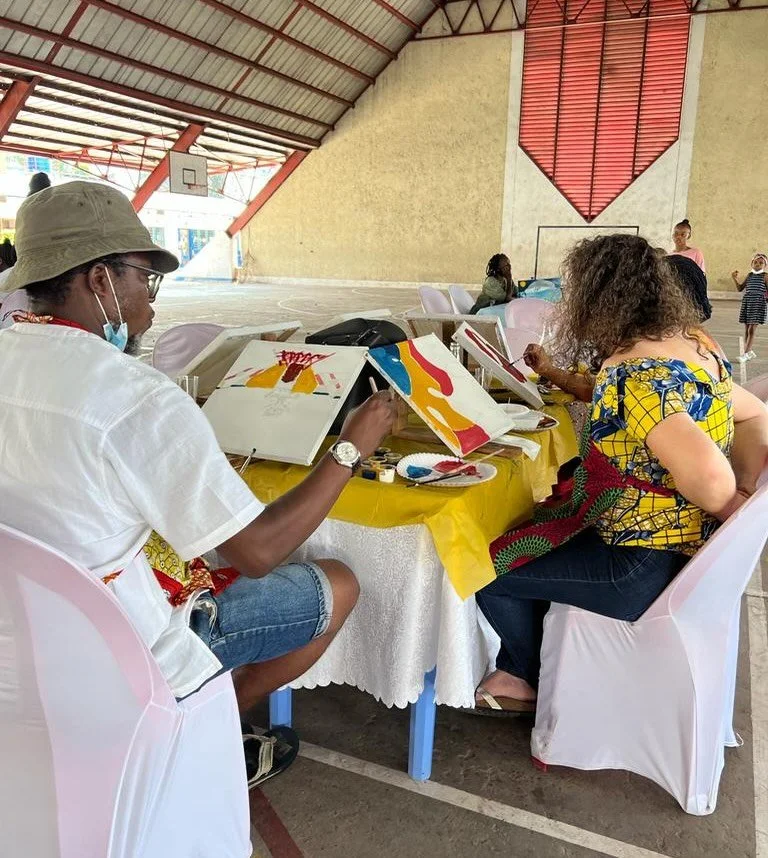 People sitting at a table doing abstract painting under a covered basketball court.