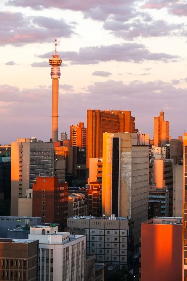 City skyline of Johannesburg, South Africa during sunset with tall buildings and a communication tower.