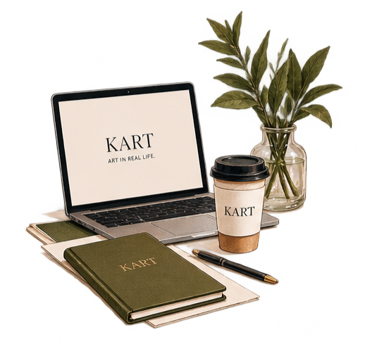 Work desk with a closed green notebook, a laptop displaying 'KART ART IN REAL LIFE', a paper coffee cup with 'KART', a black pen, and a glass vase with green leafy branches.
