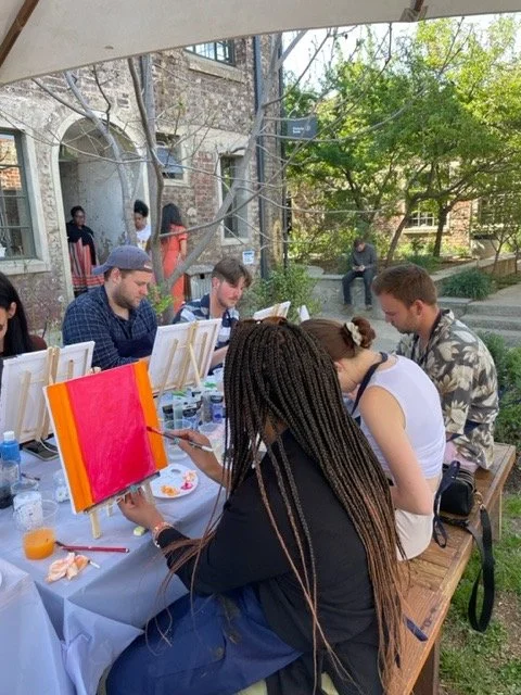 Group of people painting on canvases outdoors at a sunny gathering.