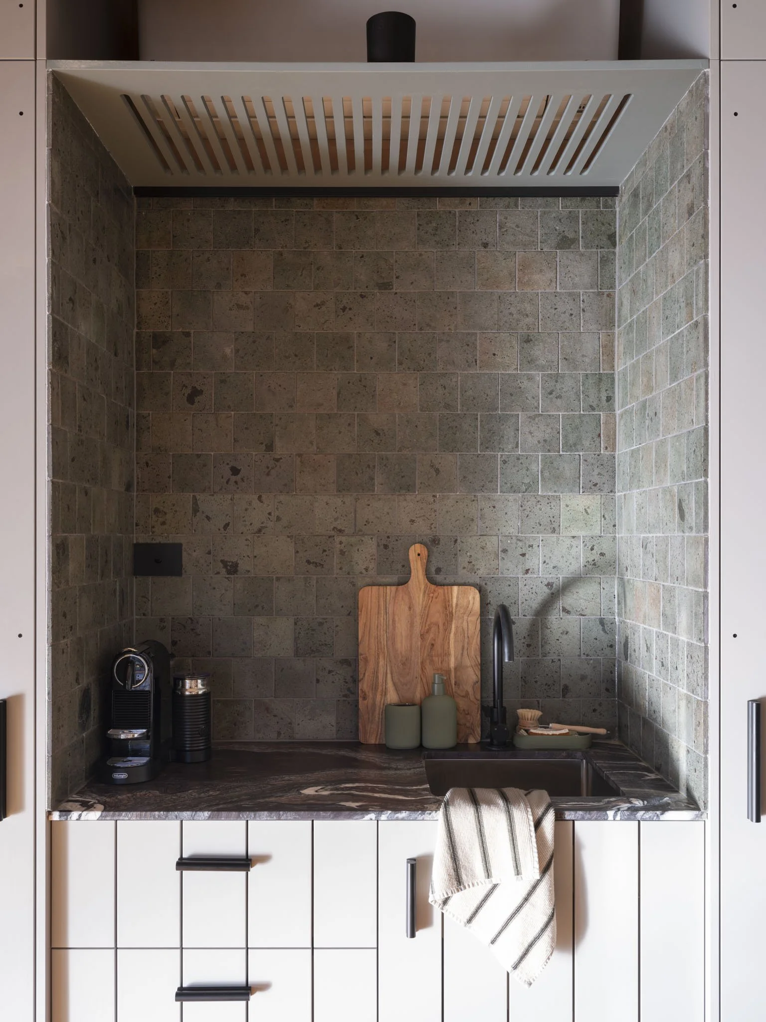 The Five Songs guest room's kitchenette with marble countertop and a wood charcuterie board, soap, and kitchen sink, white cabinets, backsplash with natural stone tiles, various kitchen tools and appliances. #SlowMornings #RusticLuxury #RelaxAndRecha