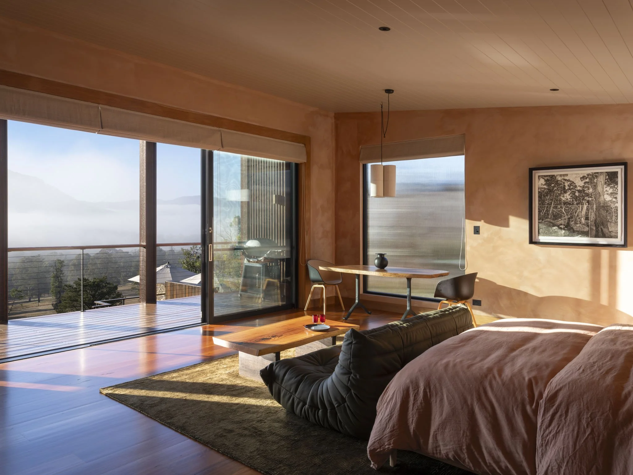 Interior of a modern designer living room with large glass sliding doors, lime washed walls, and a native timber floor. There is an olive green leather sofa with terracotta cushions, a handcrafted blackbutt slab coffee table with a tray and vintage r