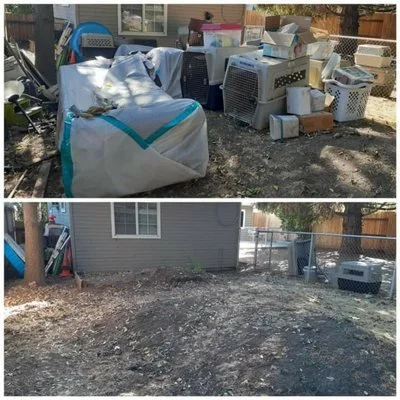 A yard with a pile of discarded furniture, electronics, and household items on the grass, and an empty dirt area in the background.