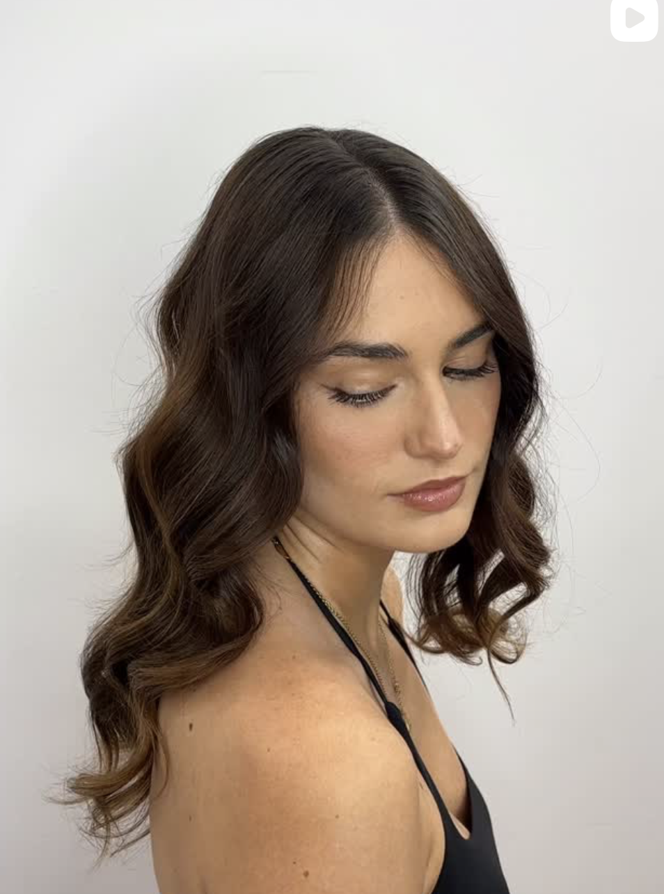 A young woman with wavy brown hair and light skin, looking down with her eyes closed, against a plain white background.