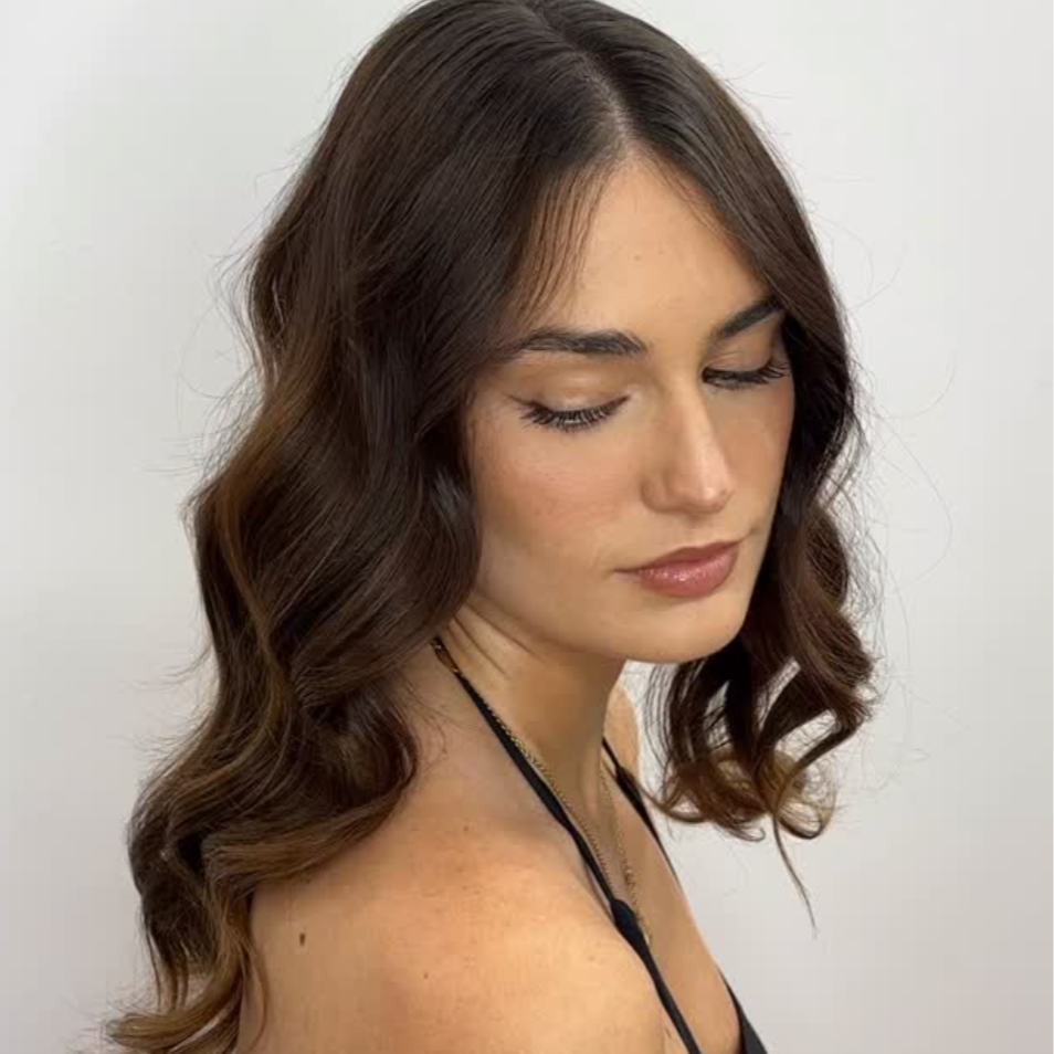 A woman with wavy brown hair and light skin, looking downward against a plain white background
