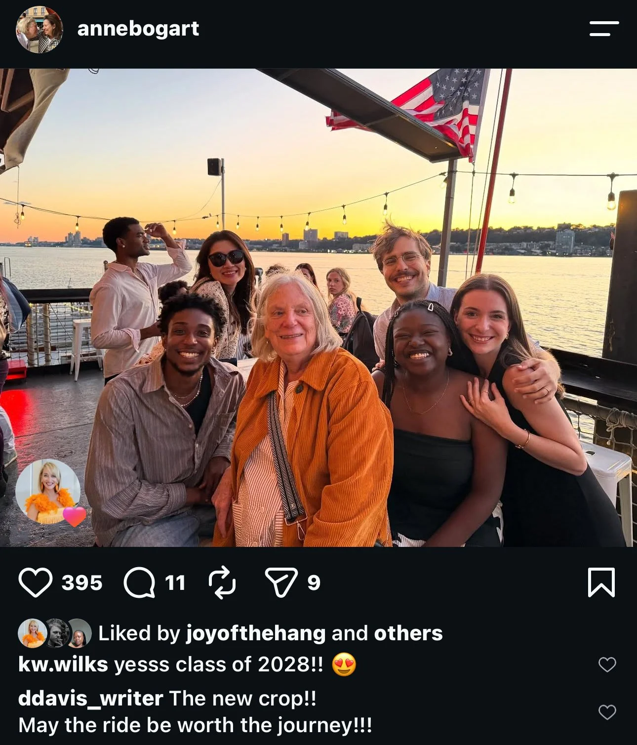 A group of eight people smiling and posing together on a boat deck with a river and city skyline in the background during sunset. The group includes a variety of ages and ethnicities, and they seem happy and enjoying their time.