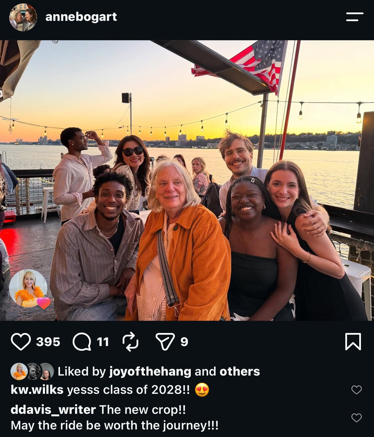 A group of eight people smiling and posing together on a boat deck with a river and city skyline in the background during sunset. The group includes a variety of ages and ethnicities, and they seem happy and enjoying their time.