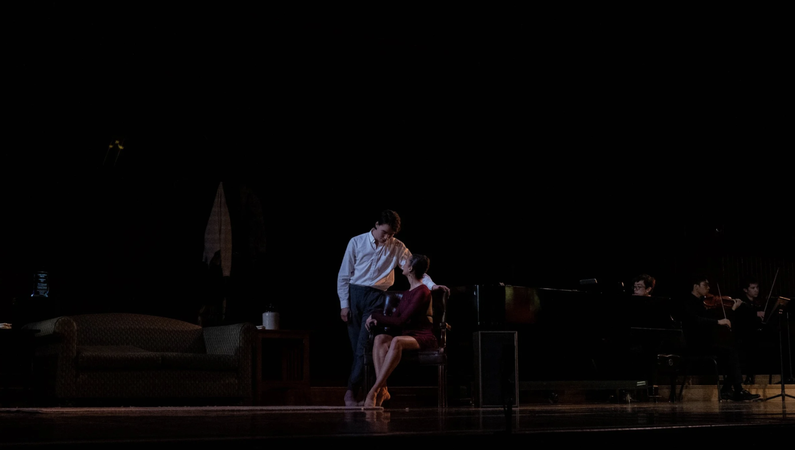 People performing on stage with a piano and string musicians in the background.