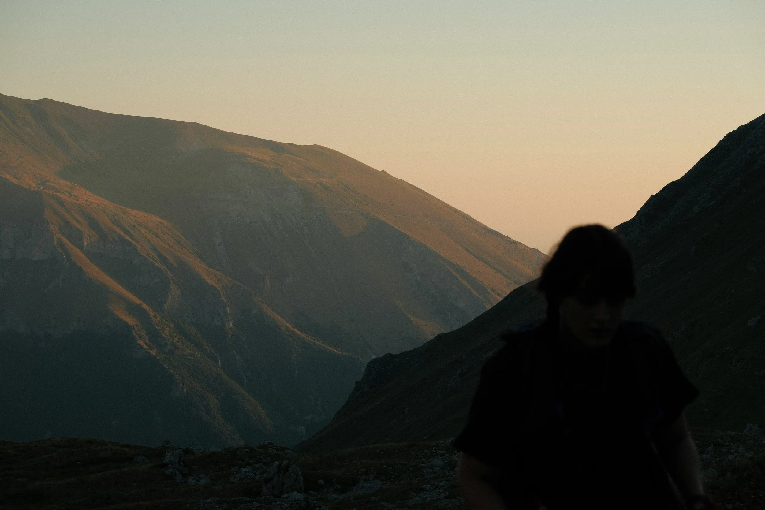 Sunset over mountains with a person sitting in the foreground.