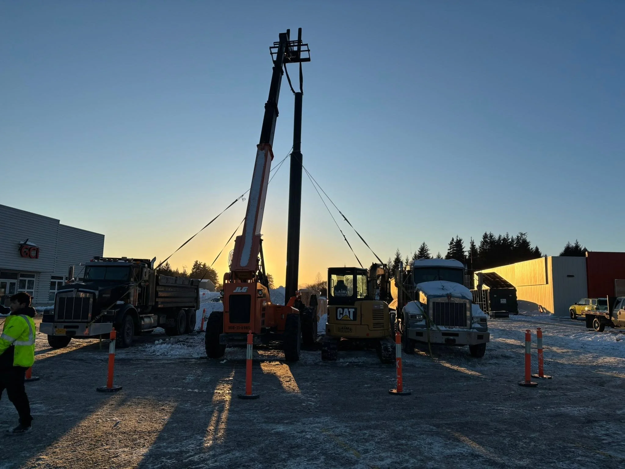 Construction crew using heavy equipment to install a tall steel column at a snowy job site.
