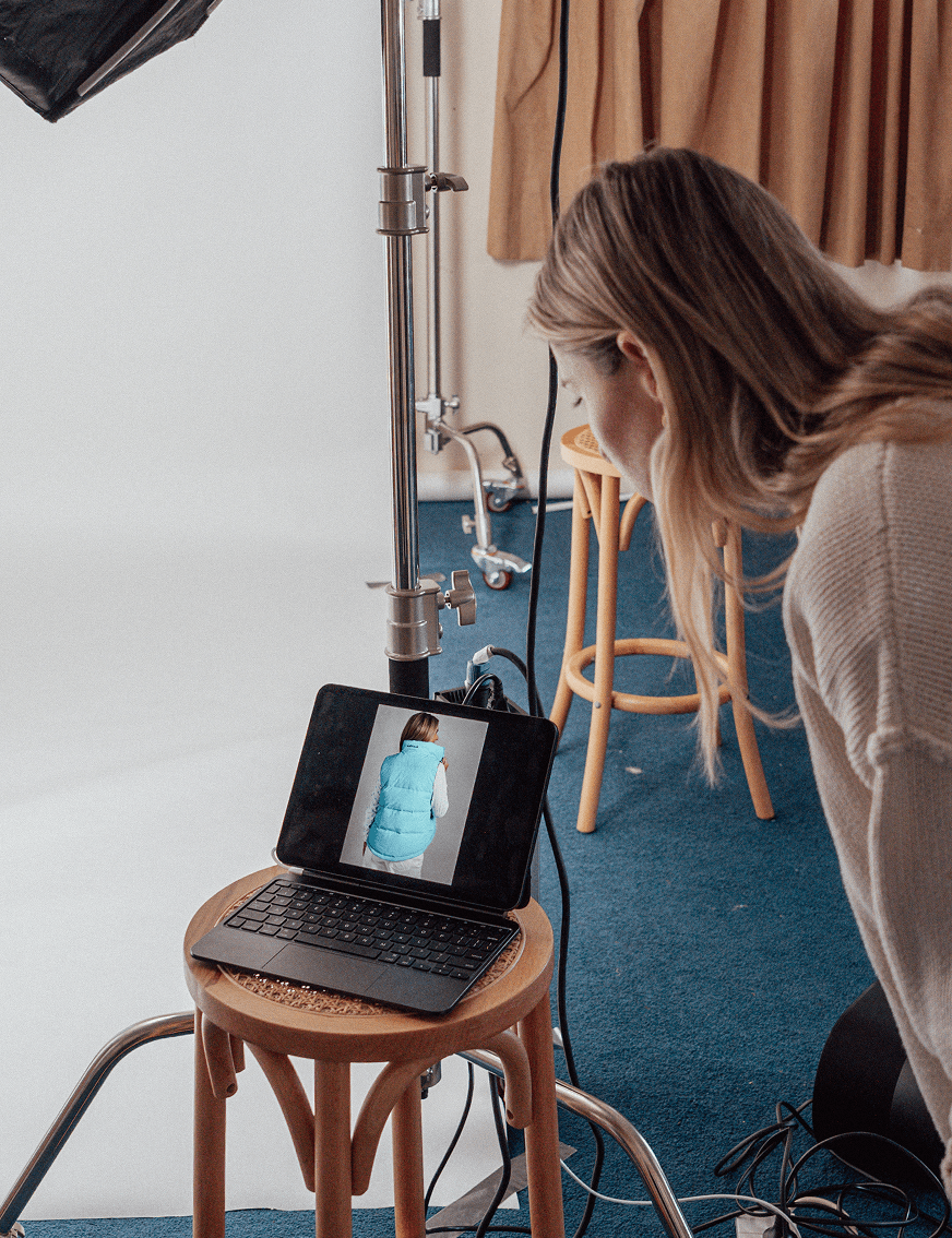 Woman looking at a tablet on a wooden stool, showing a picture of a person wearing a blue puffer vest.