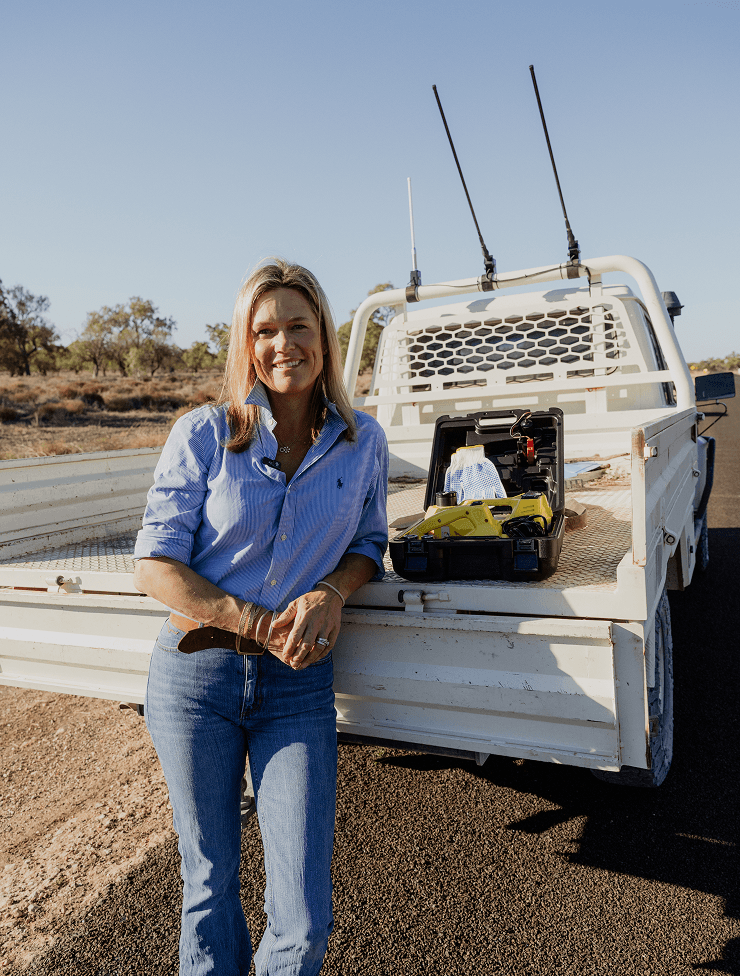 A woman standing next to a white utility truck with equipment in the bed, outdoors on a clear day.