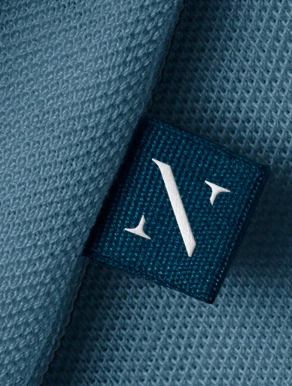 Close-up of a clothing label sewn into a blue fabric garment, displaying the Ninety logo.