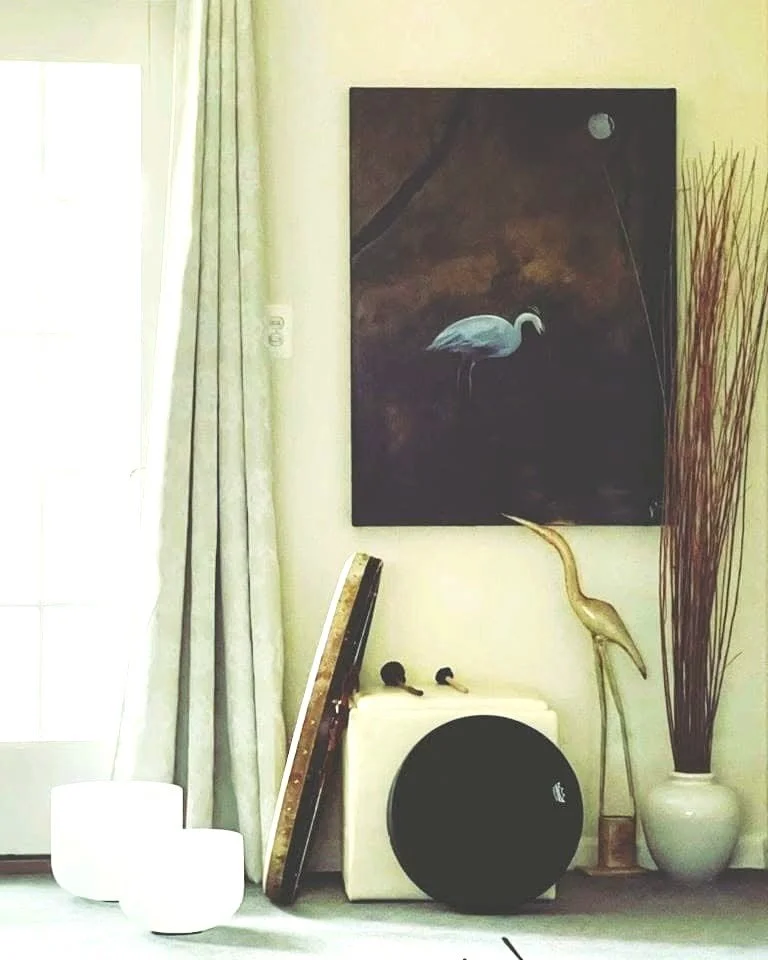 Reiki studio room with a heron painting, bird sculpture, tall vase of reeds, hand-held drum, framed artwork, and white candleholders.