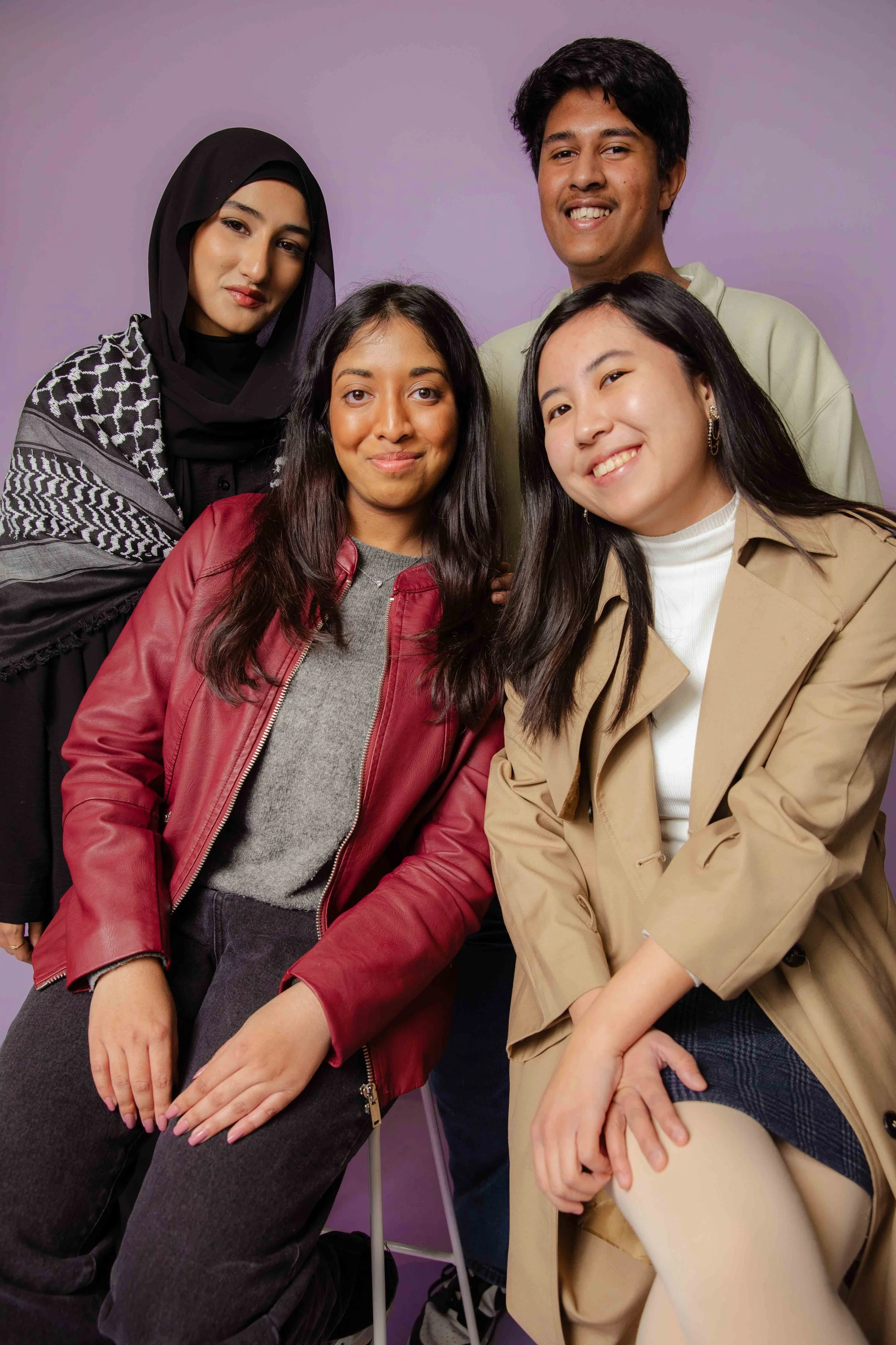 Group of five diverse young adults posing together against a purple background, smiling.